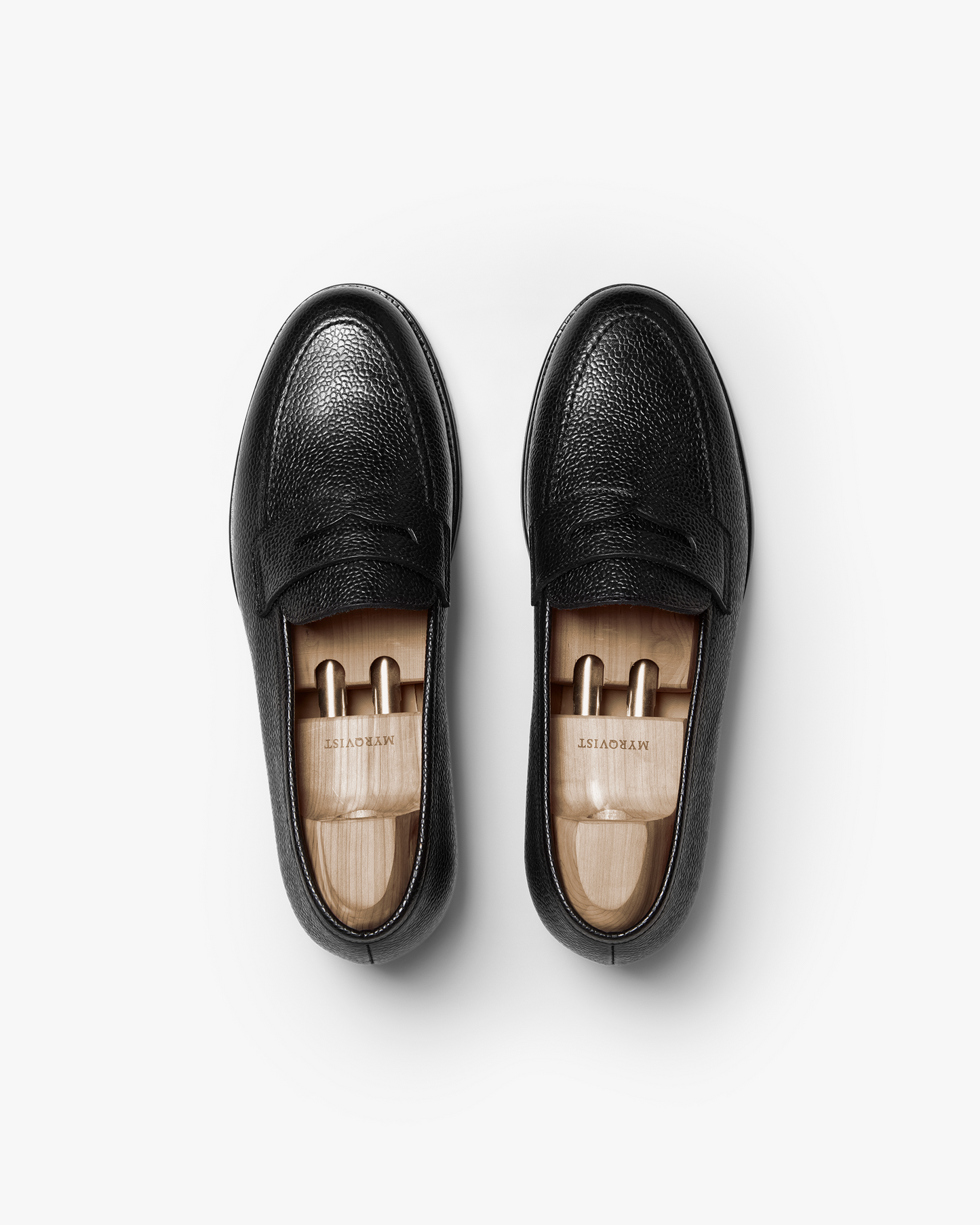A top-down studio shot of a pair of Stenhammar II – Black Country Calf loafers with wooden shoe trees, on a white background.
