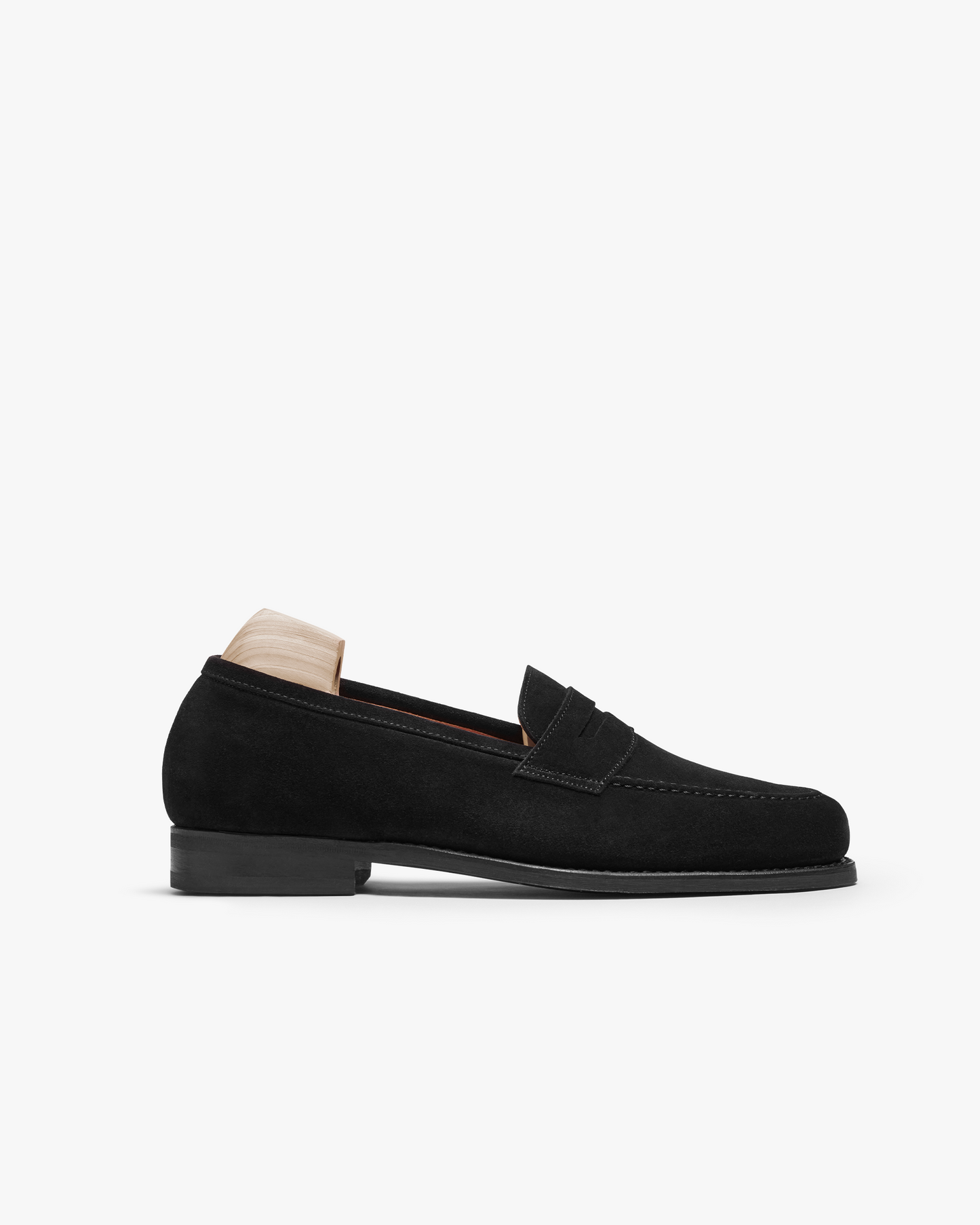 A side profile view of Stenhammar II – Black Suede, an apron-fronted penny loafer with a full rubber sole.