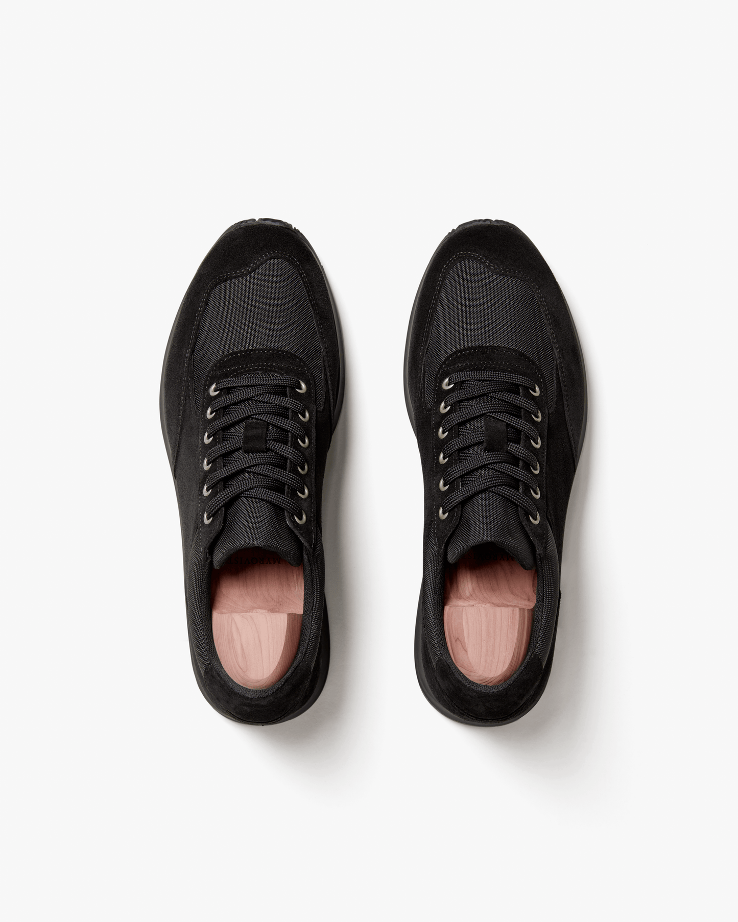Overhead view of a pair of Stensund – Black Suede trainers with wooden shoe trees on a white background.