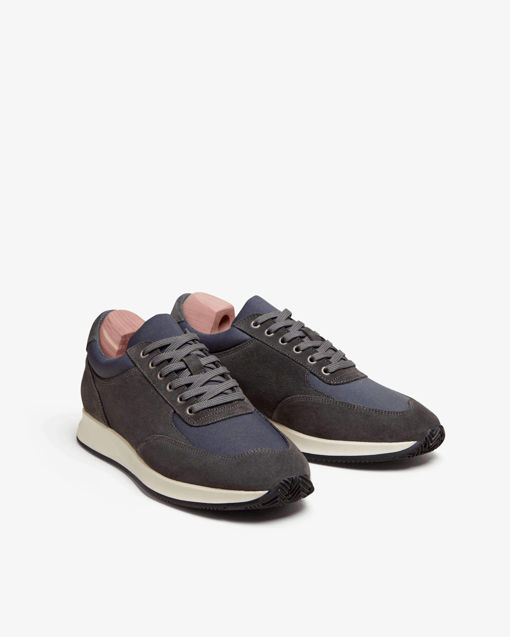 A pair of Stensund – Dark Grey Suede sneakers with wooden shoe trees, shot against a white studio background.