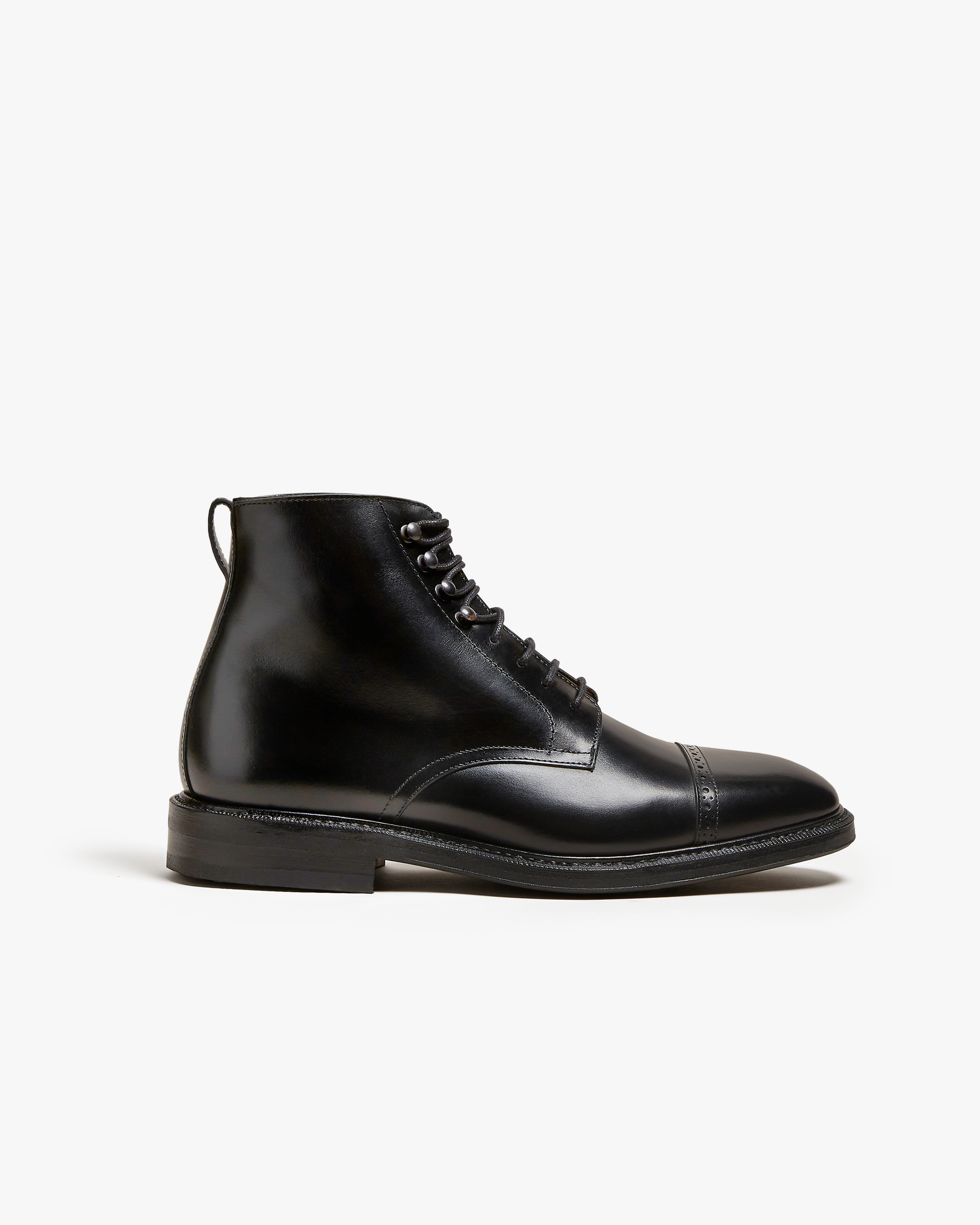 A profile view of the Tjärnö – Black Calf jumper boot, detailing its black calf leather and punched toe cap.
