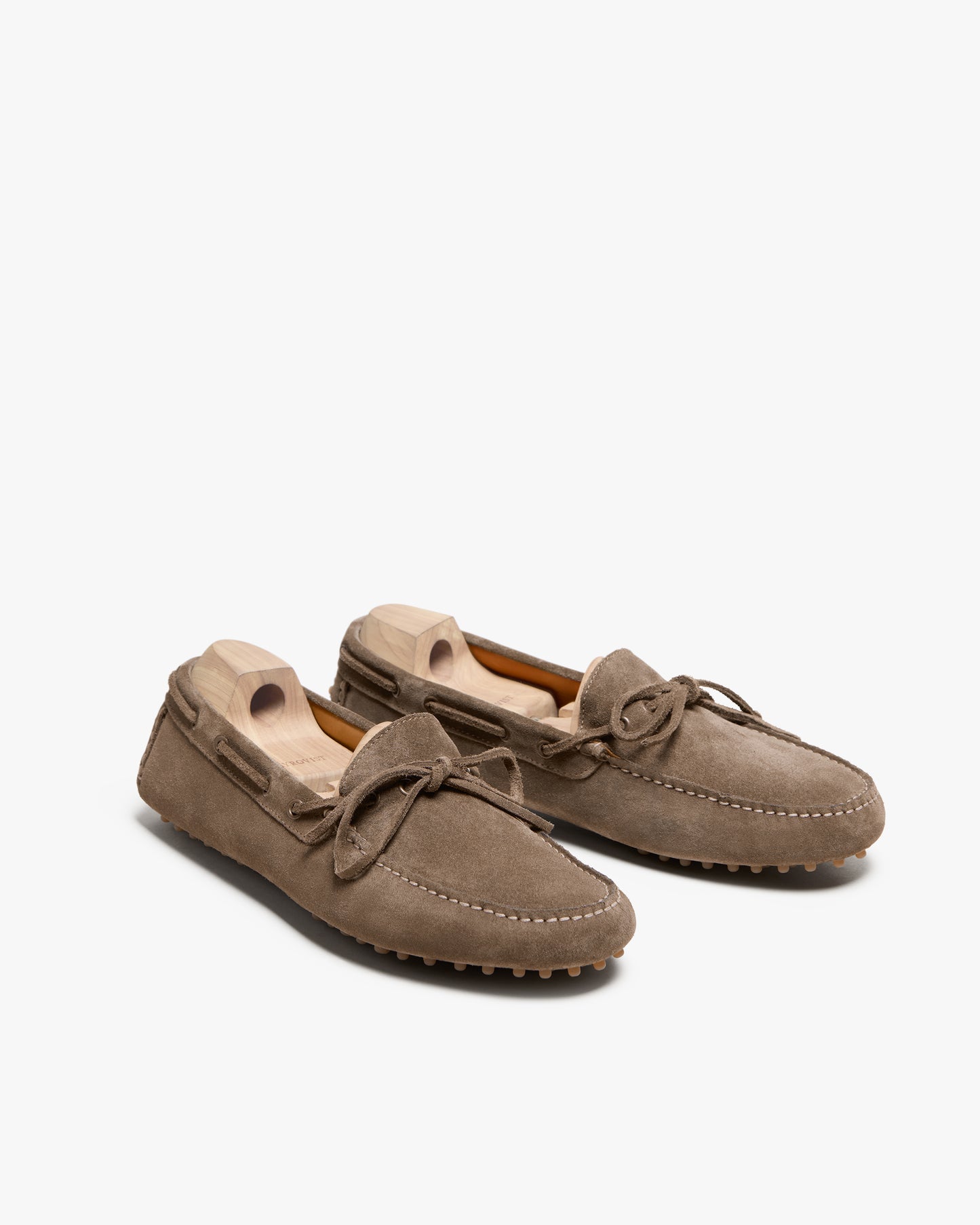 A pair of Tofta – Taupe Suede driving shoes with wooden shoe trees on a white background.