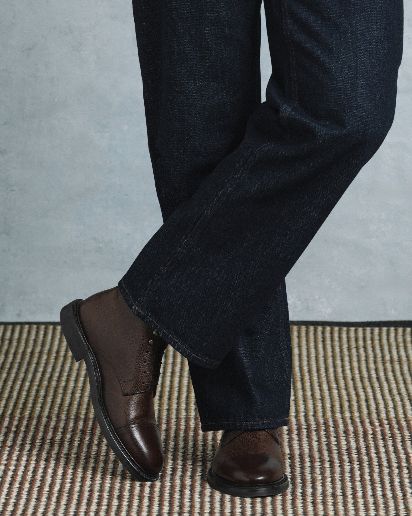 Abisko in dark brown country calf worn with dark denim, showcasing the textured grained leather, cap toe, and sturdy rubber sole for a refined yet versatile style suitable for both casual and dressed-up occasions.
