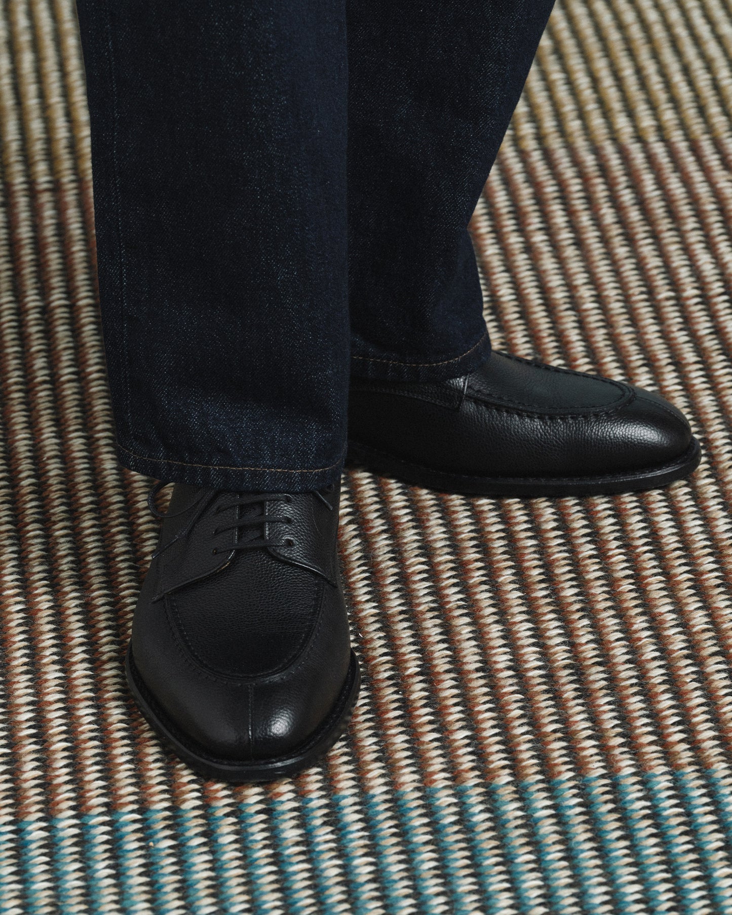 Norrmalm II in black hatch grain worn with dark denim trousers, highlighting the textured split toe derby design and versatile styling for both formal and business casual looks.