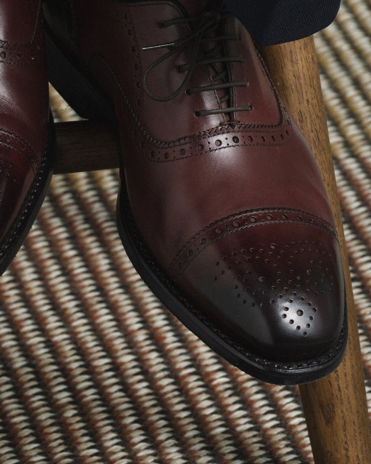 Close-up of Strömsö II in dark mahogany calf, showcasing the semi-brogue Oxford’s detailed cap toe perforations and rich brown leather, styled with tailored slacks.