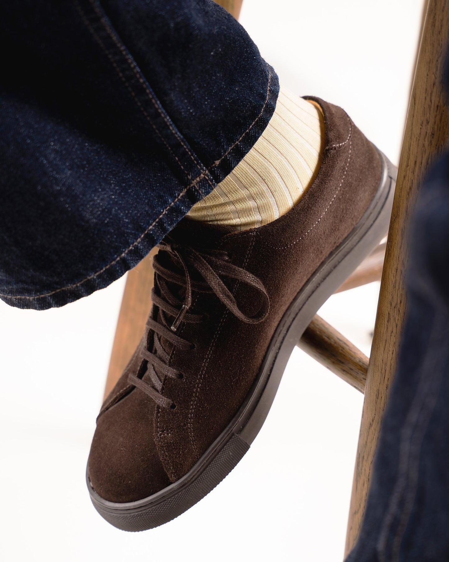 A close-up of a person wearing Axel – Cotton Socks – Pineapple Yellow with dark brown suede sneakers and blue jeans.