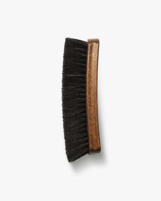An overhead view of the Shoe Brush – Myrqvist, showing its brown varnished wooden handle and dense black horsehair bristles.