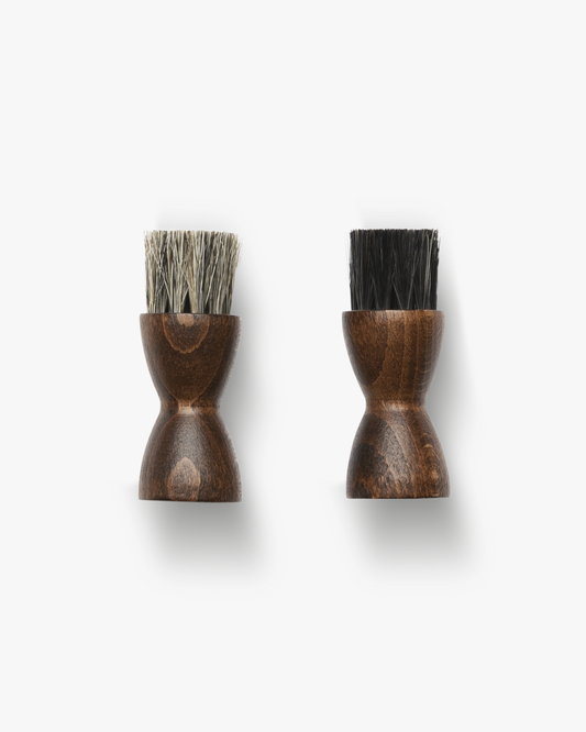 A top-down view of two Jar Brushes with dark wooden handles, one featuring light bristles and the other dark bristles.