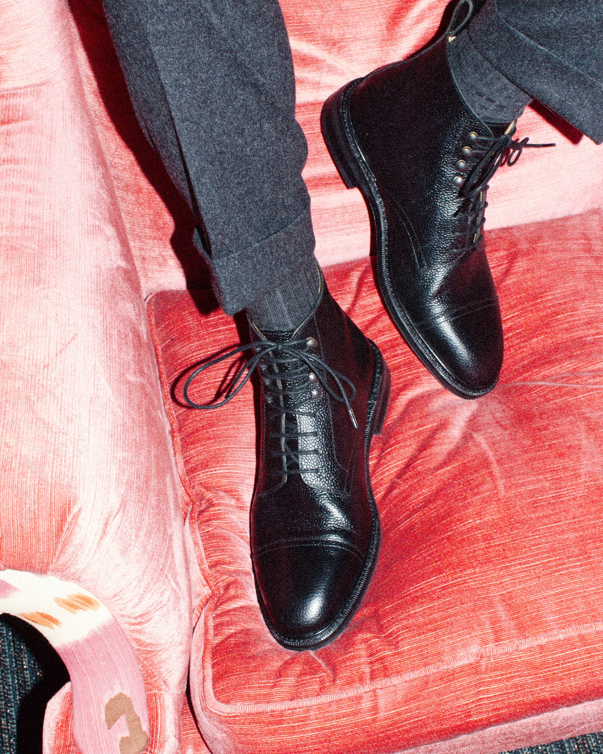 An overhead view of a person wearing Abisko – Black Country Calf boots with grey wool trousers on a pink sofa.