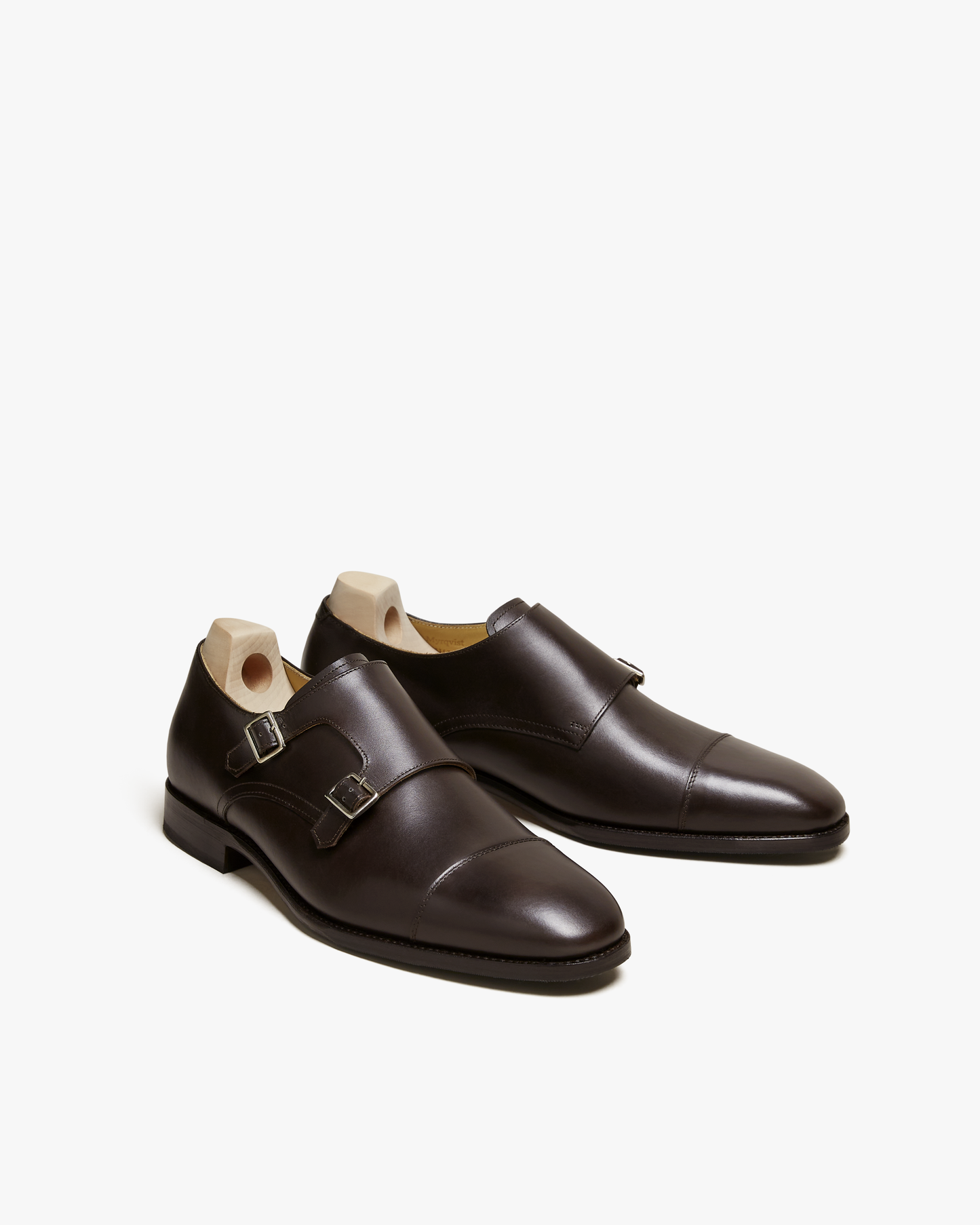 A pair of Ålsten – Dark Brown Calf, a cap toe double monk strap shoe, shown with shoe trees against a white background.