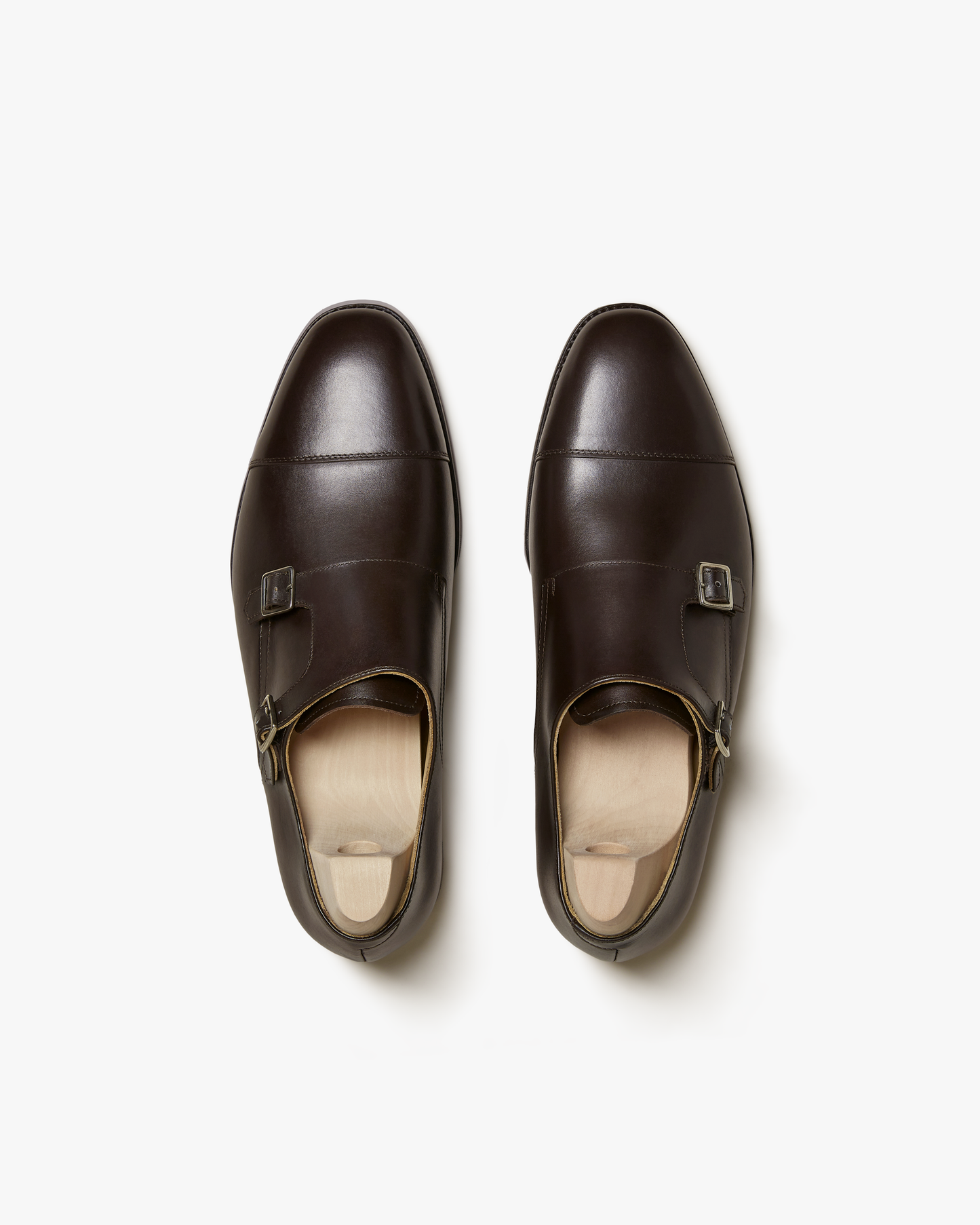 Top-down view of Ålsten – Dark Brown Calf, cap toe double monk straps with shoe trees on a white backdrop.