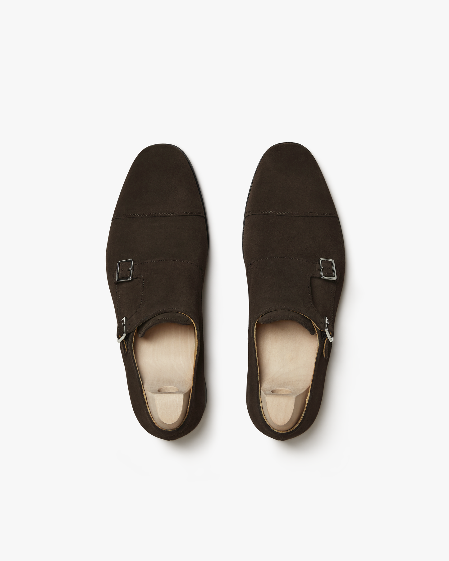 A top-down studio shot of a pair of Ålsten – Dark Brown Suede double monk strap shoes with shoe trees.