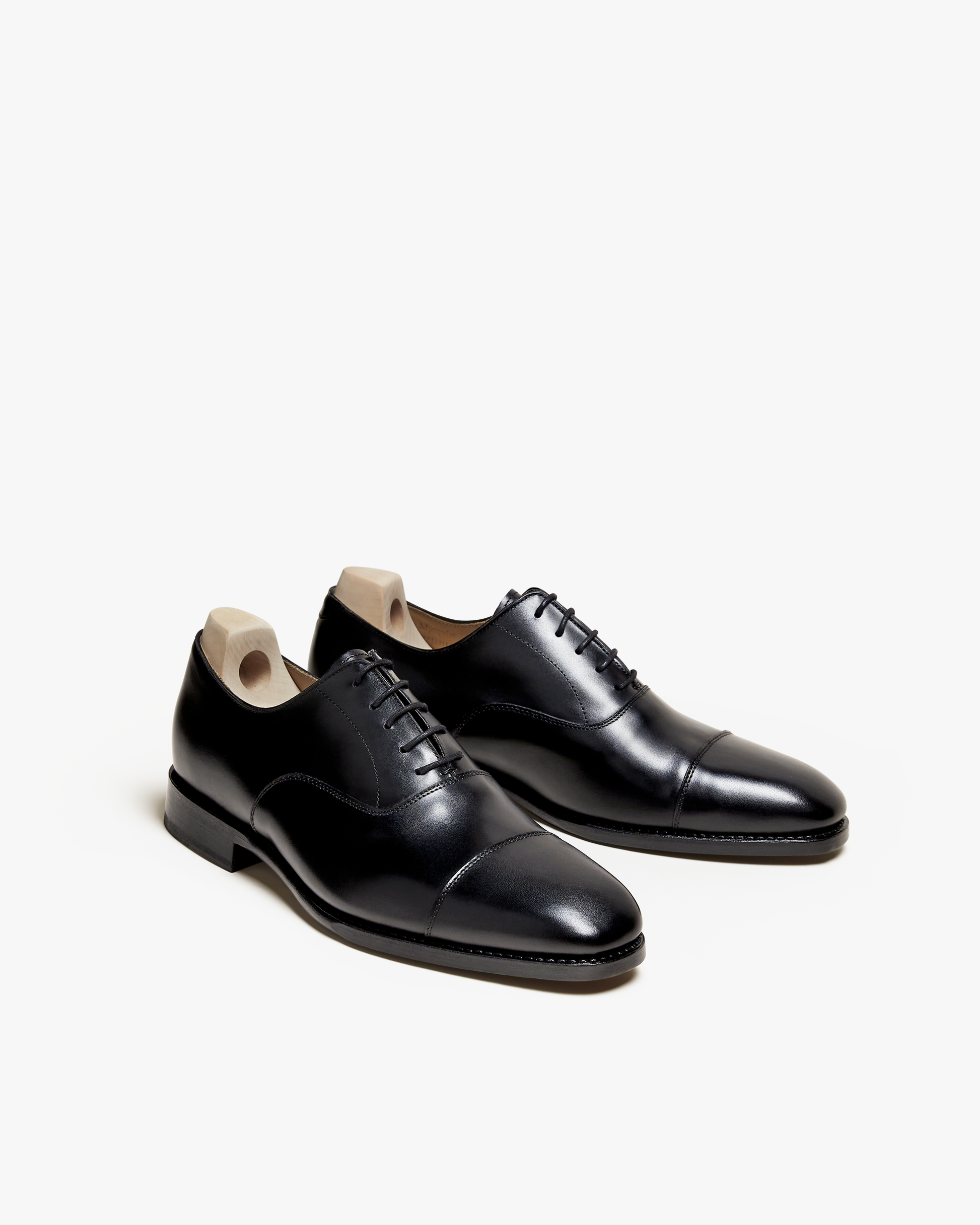 A pair of Äppelviken – Black Calf cap toe Oxfords with shoe trees, displayed at a three-quarter angle on a white background.