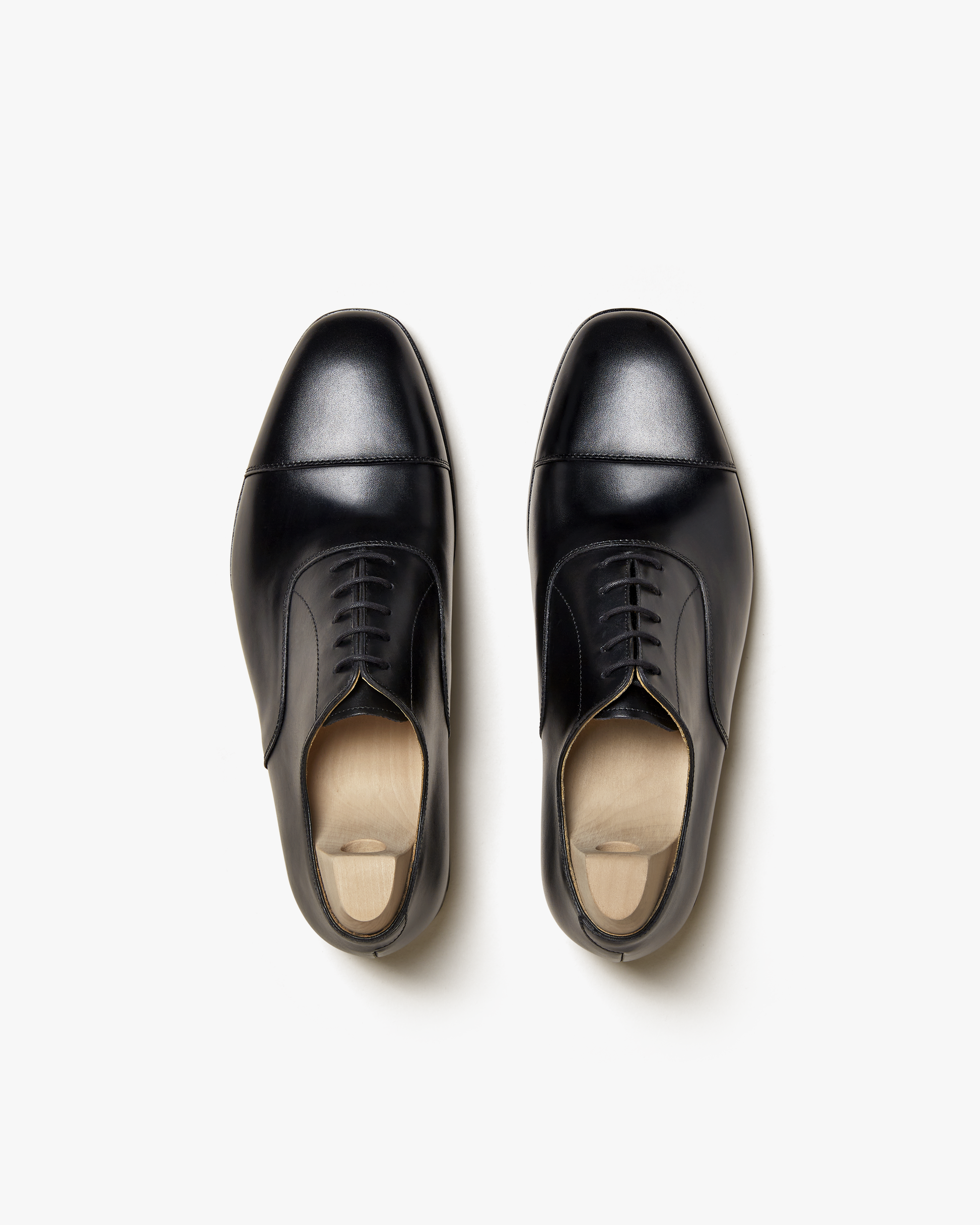 Overhead view of a pair of Äppelviken – Black Calf Oxford shoes with wooden shoe trees on a white background.