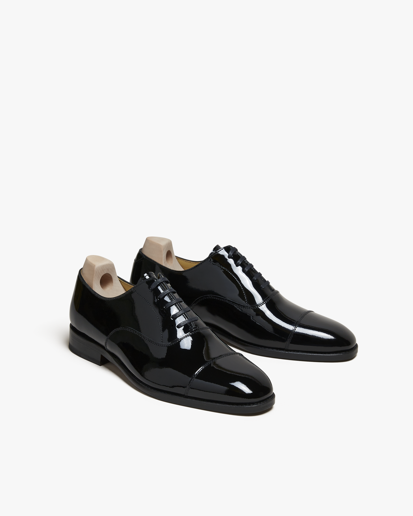 A pair of Vinterviken – Black Patent Leather oxfords with wooden shoe trees, against a white studio background.