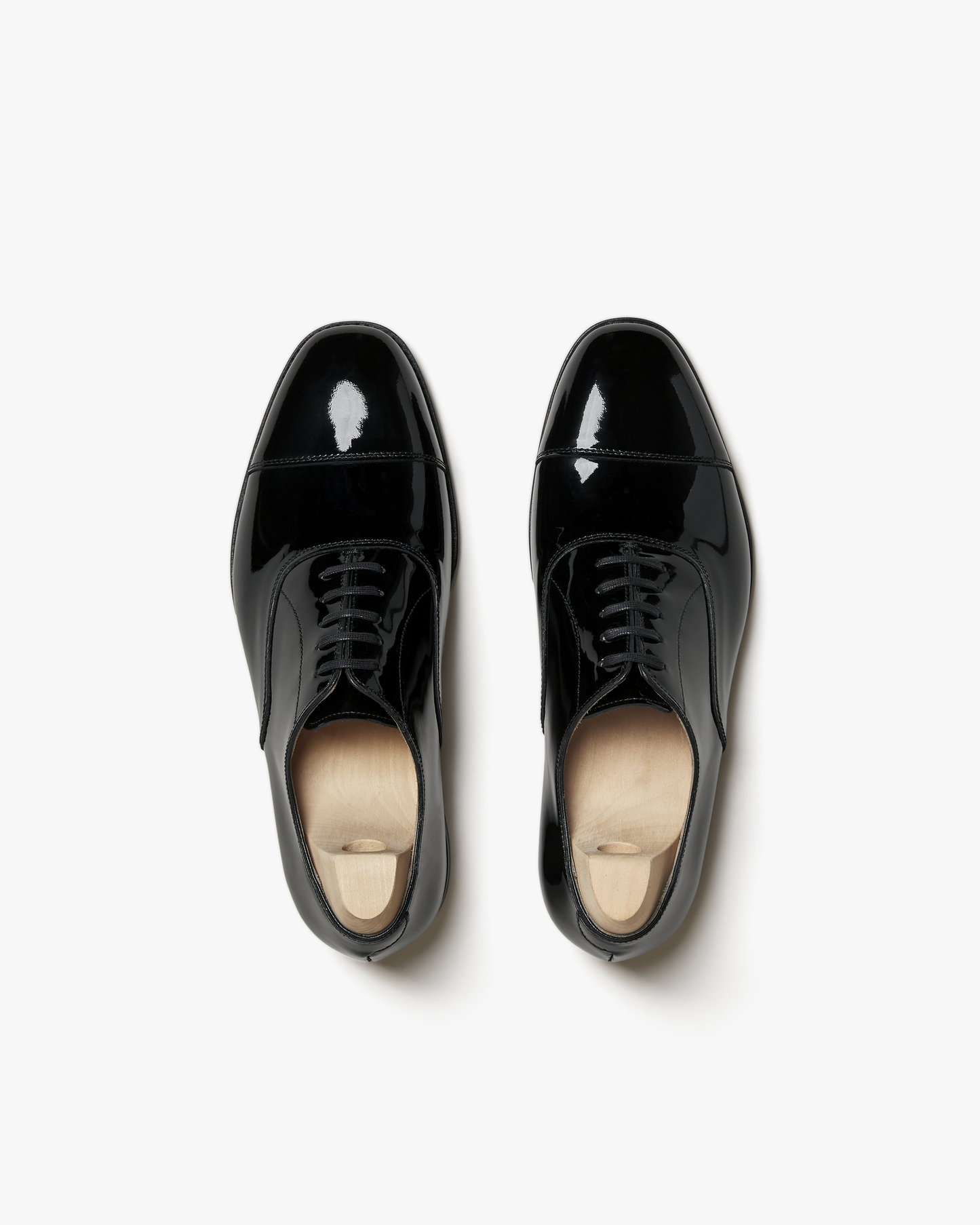 A top-down view of Vinterviken – Black Patent Leather, a pair of oxford shoes with shoe trees on a white background.