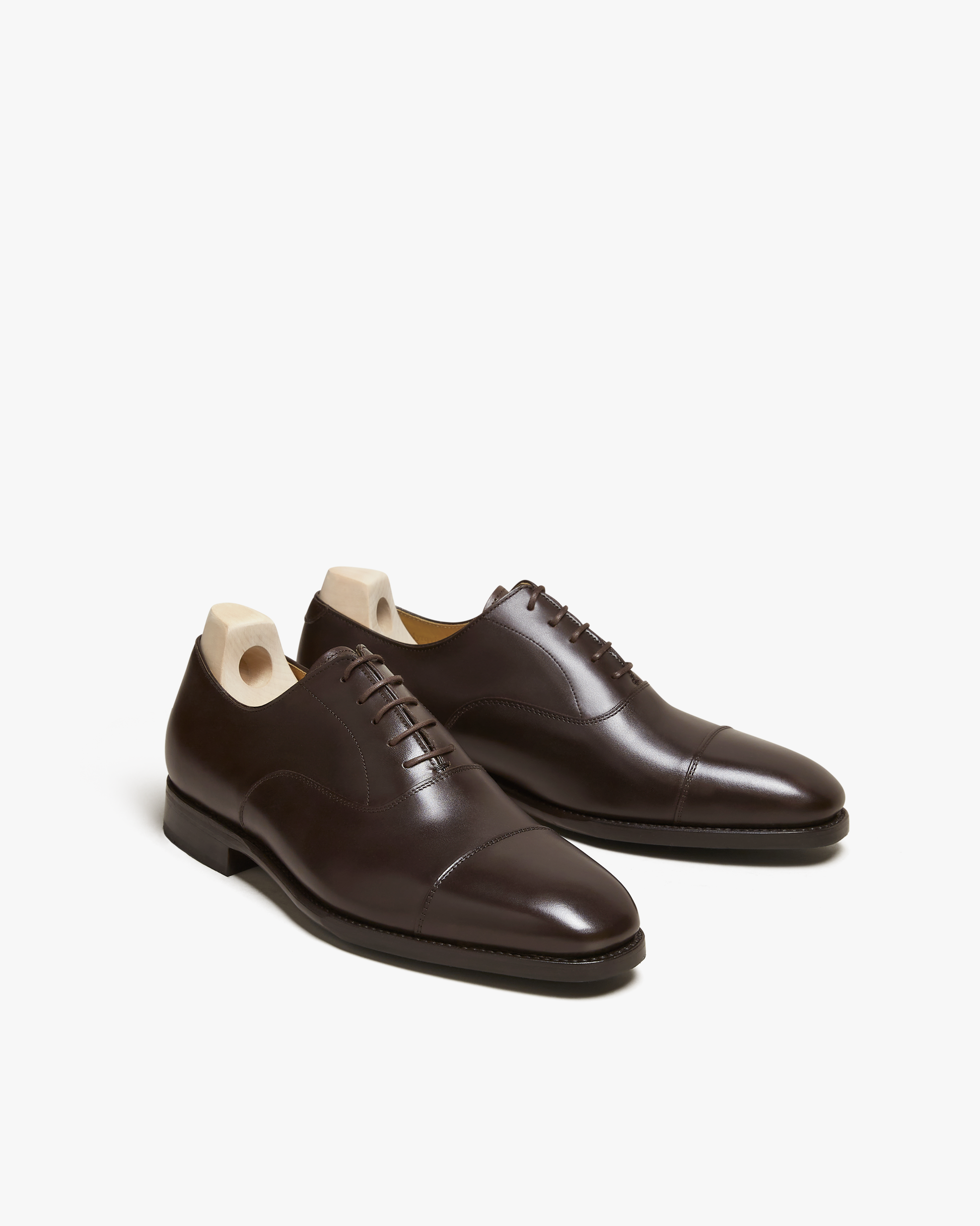 A pair of Äppelviken – Dark Brown Calf oxford shoes with shoe trees, shot from a three-quarter angle on a white background.