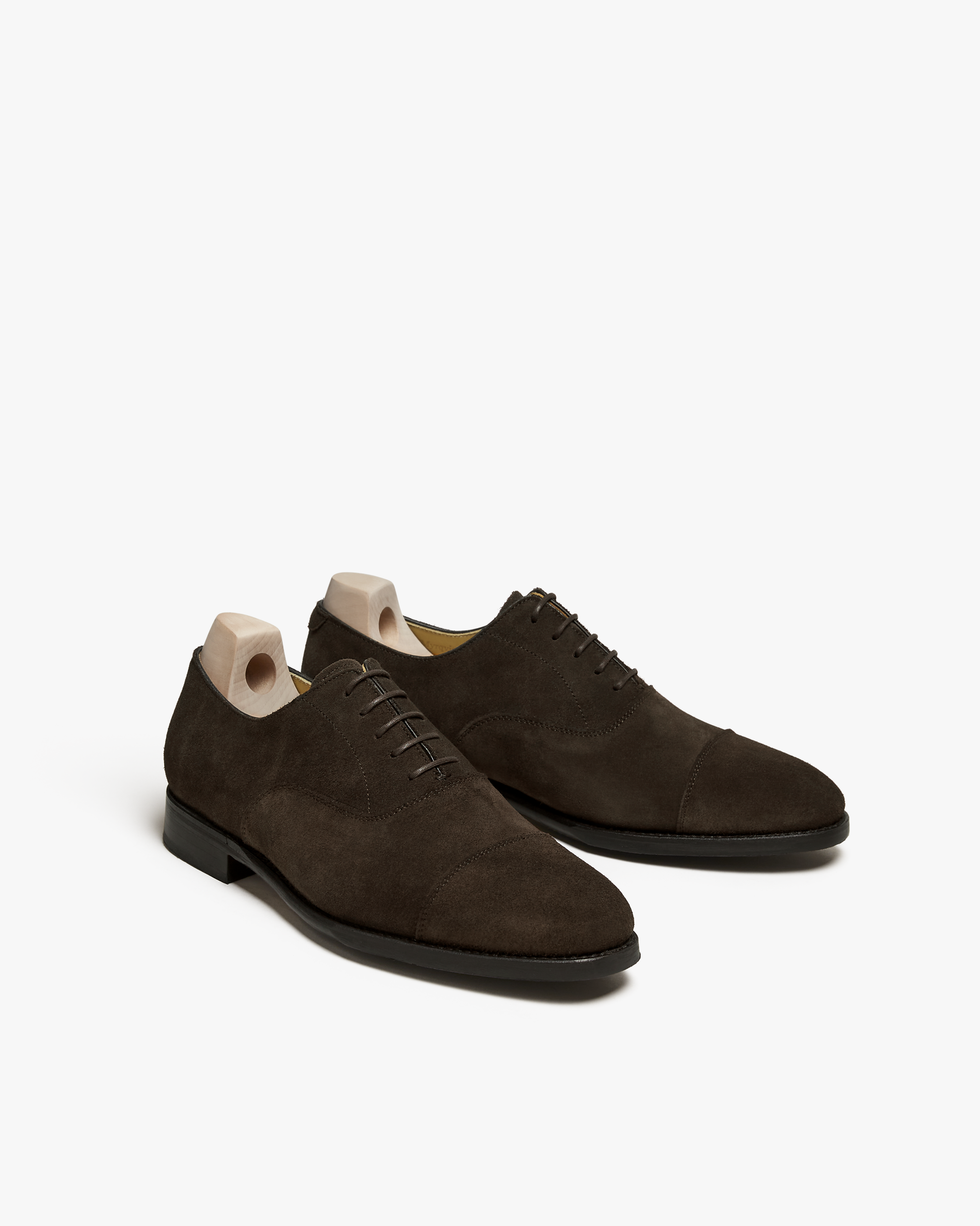 Three-quarter view of a pair of Äppelviken – Dark Brown Suede Oxfords with shoe trees, on a white studio background.