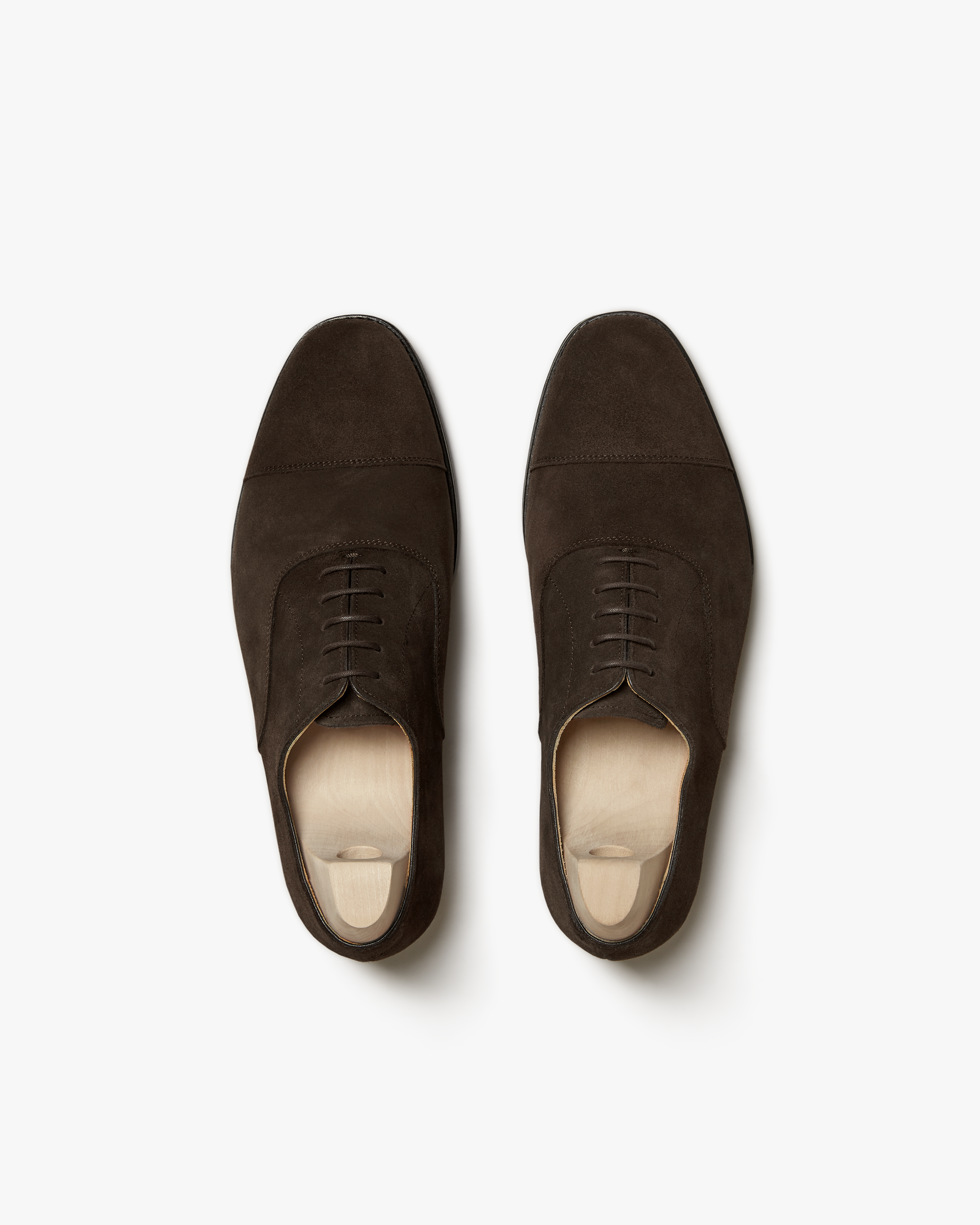 A pair of Äppelviken – Dark Brown Suede cap toe Oxford shoes with shoe trees, shot from above on a white background.