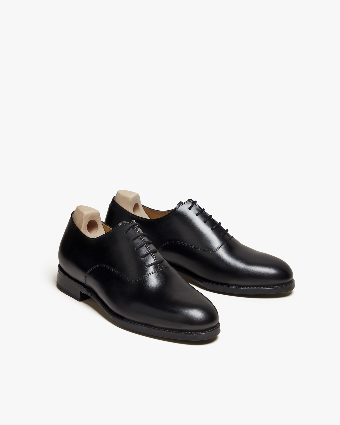 A pair of Arvika II – Black Calf oxfords with wooden shoe trees, shown from an angle on a white background.