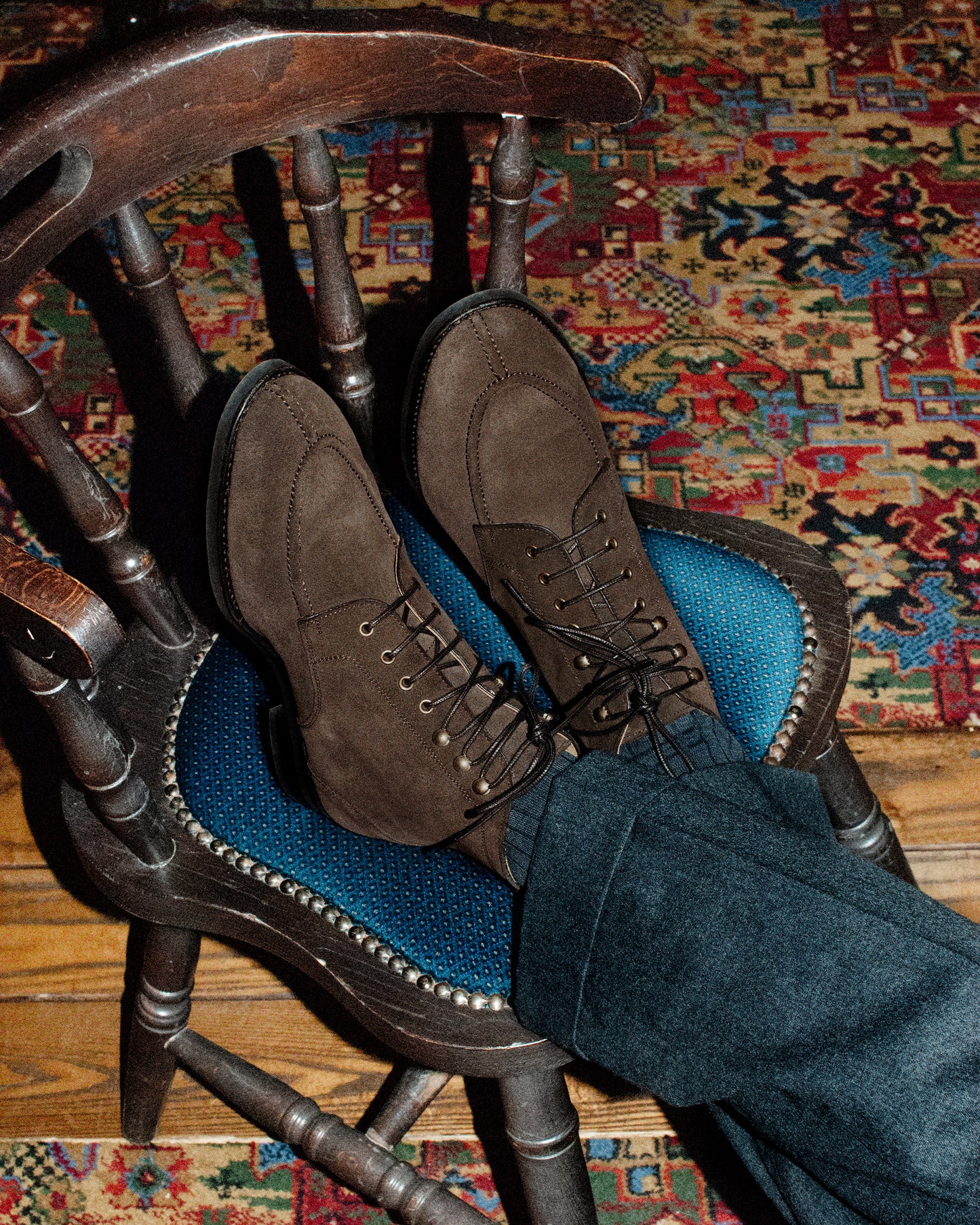 A person wearing Gothem – Dark Brown Suede boots, with their feet resting on a vintage-style chair.