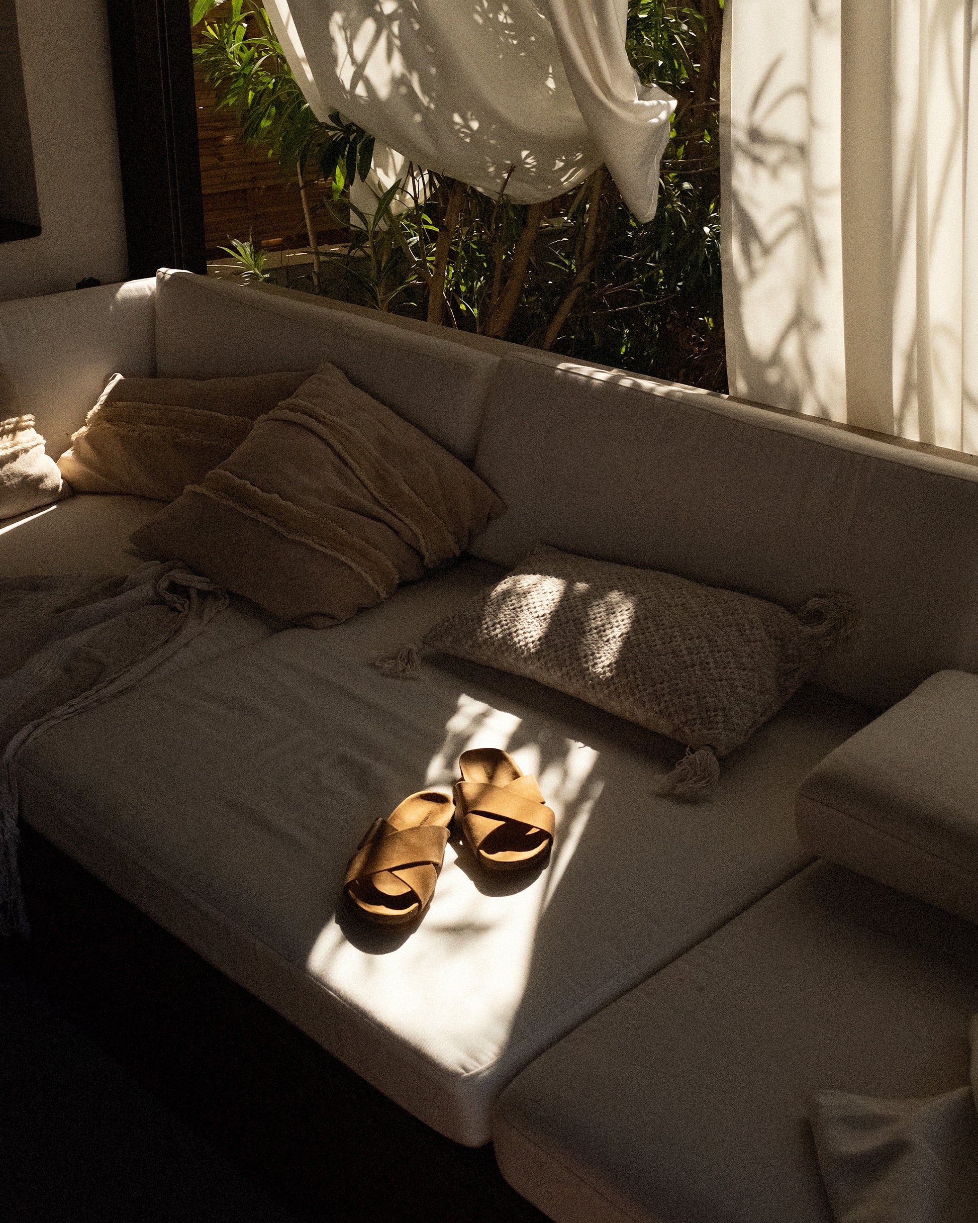 Solvik – Sand Suede sandals resting on a light-colored sofa, bathed in warm sunlight.