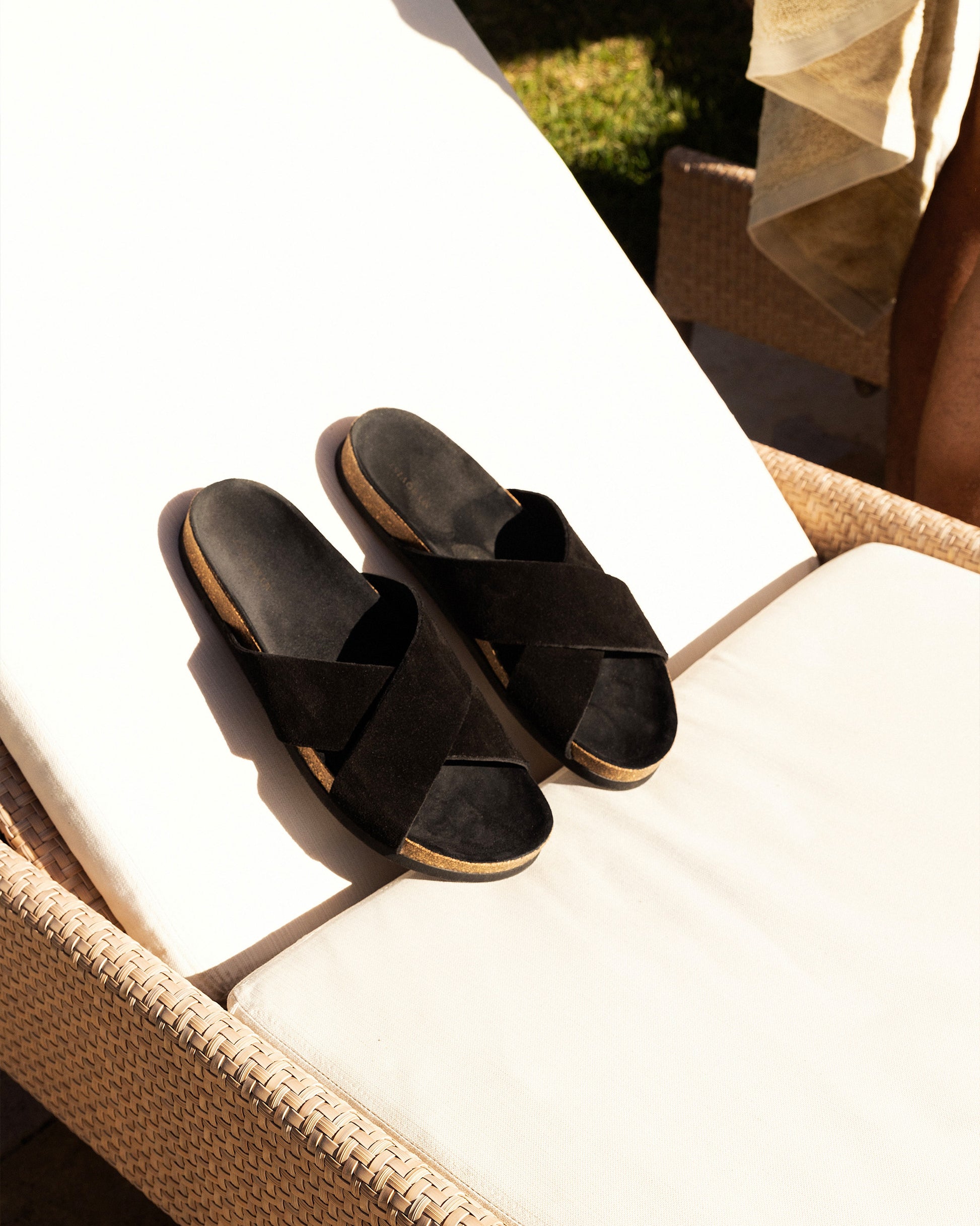Solvik – Black Suede sandals resting on a sunlit outdoor lounge chair.