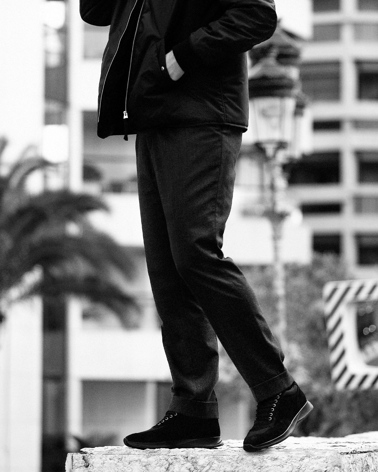 A person wearing Stensund – Black Suede trainers with dark slacks and a jacket, walking in an urban setting.