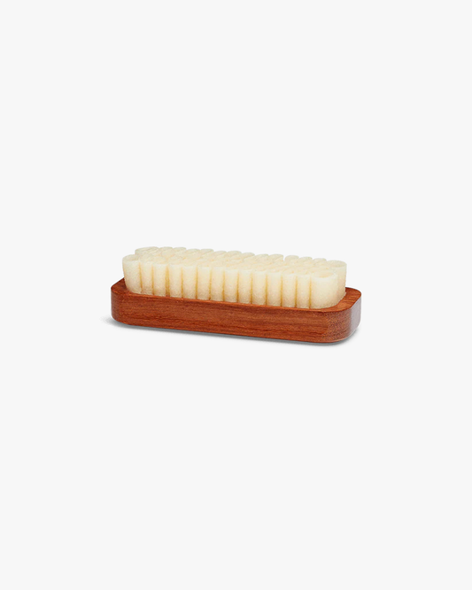 A side view of the Saphir – Crepe Brush with its wooden handle and natural crepe rubber bristles on a white background.