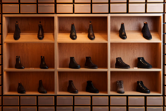 Open wooden shop shelving filled with rows of black and brown Chelsea boots and laced boots.