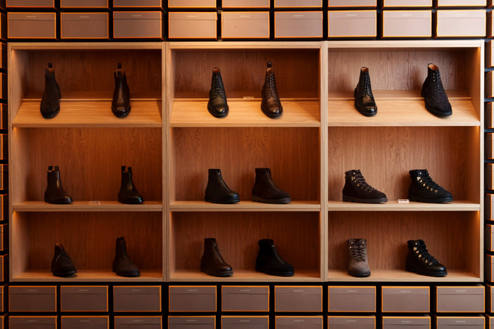 Open wooden shop shelving filled with rows of black and brown Chelsea boots and laced boots.