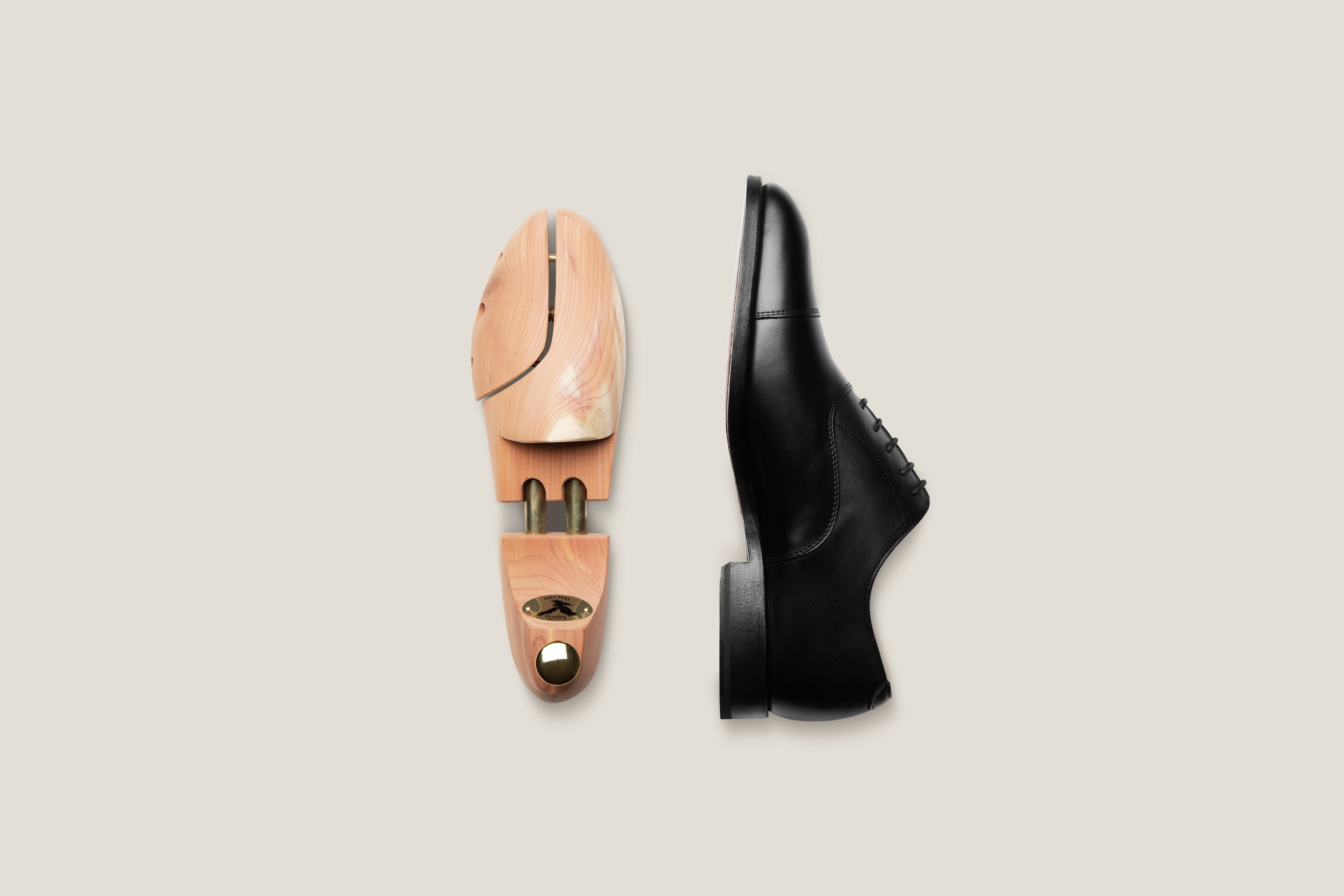A cedar wooden shoe tree beside a black patent leather oxford, arranged at an angle on a pale linen surface.