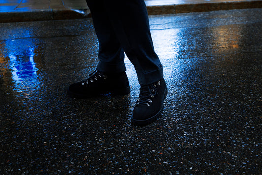 Black suede hiking boots standing on wet, reflective asphalt at dusk.