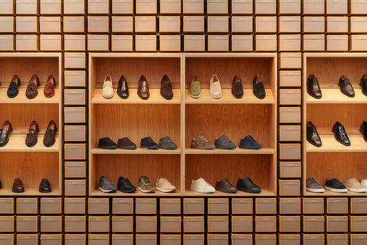 Wooden store shelving in several compartments displaying rows of leather and suede shoes in different styles, including loafers, oxfords and low sneakers.