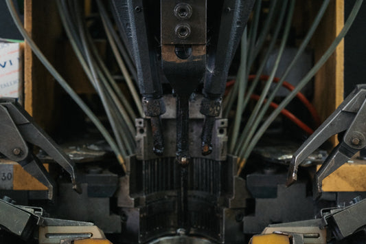 A shoemaking machine in a factory clamping a pale shoe last, with metal tooling and cables above it.