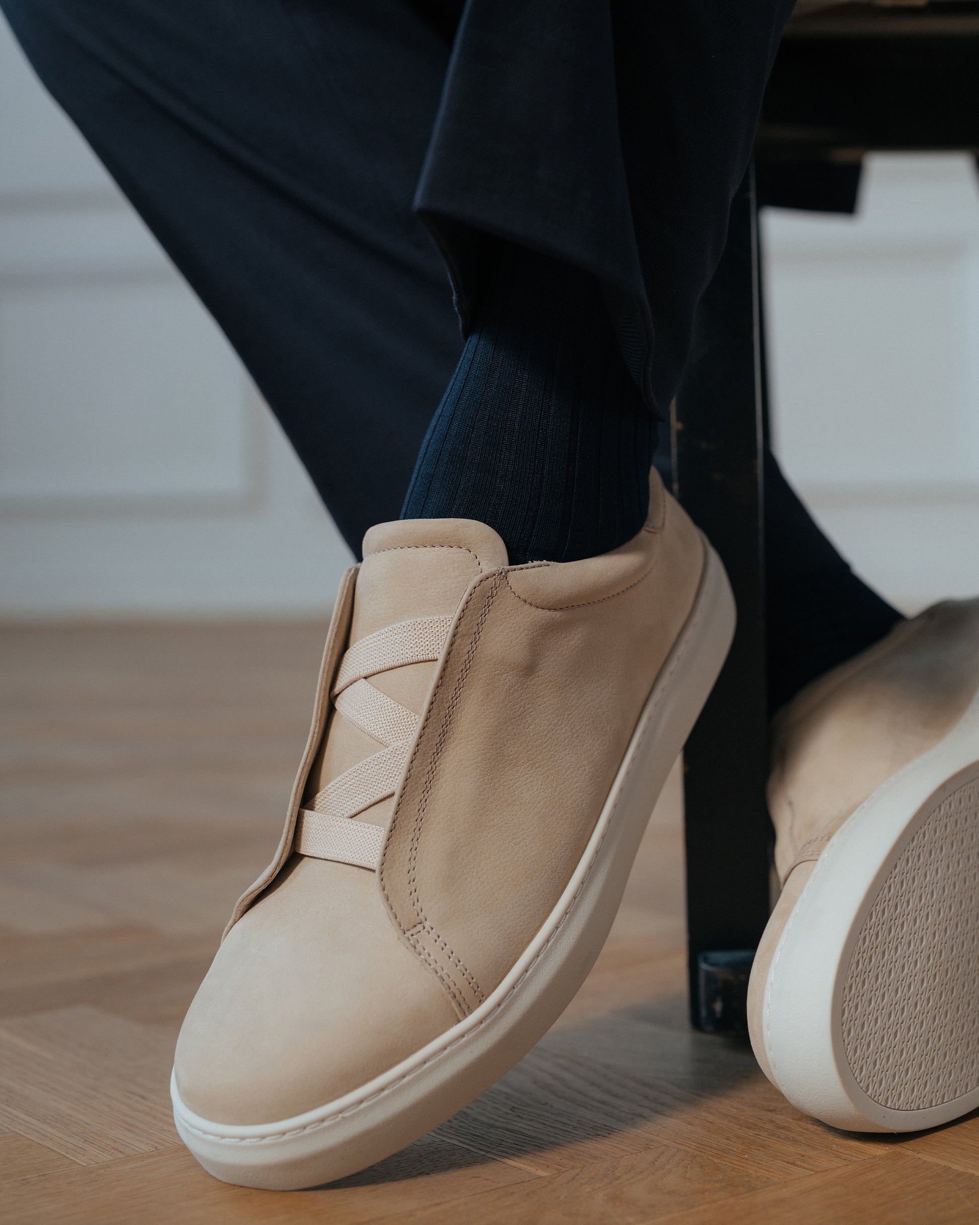 Alnö II in beige nubuck shown worn with dark trousers and socks, highlighting the minimalist slip-on design with elastic crossover and clean white sole, ideal for both business casual and relaxed settings.