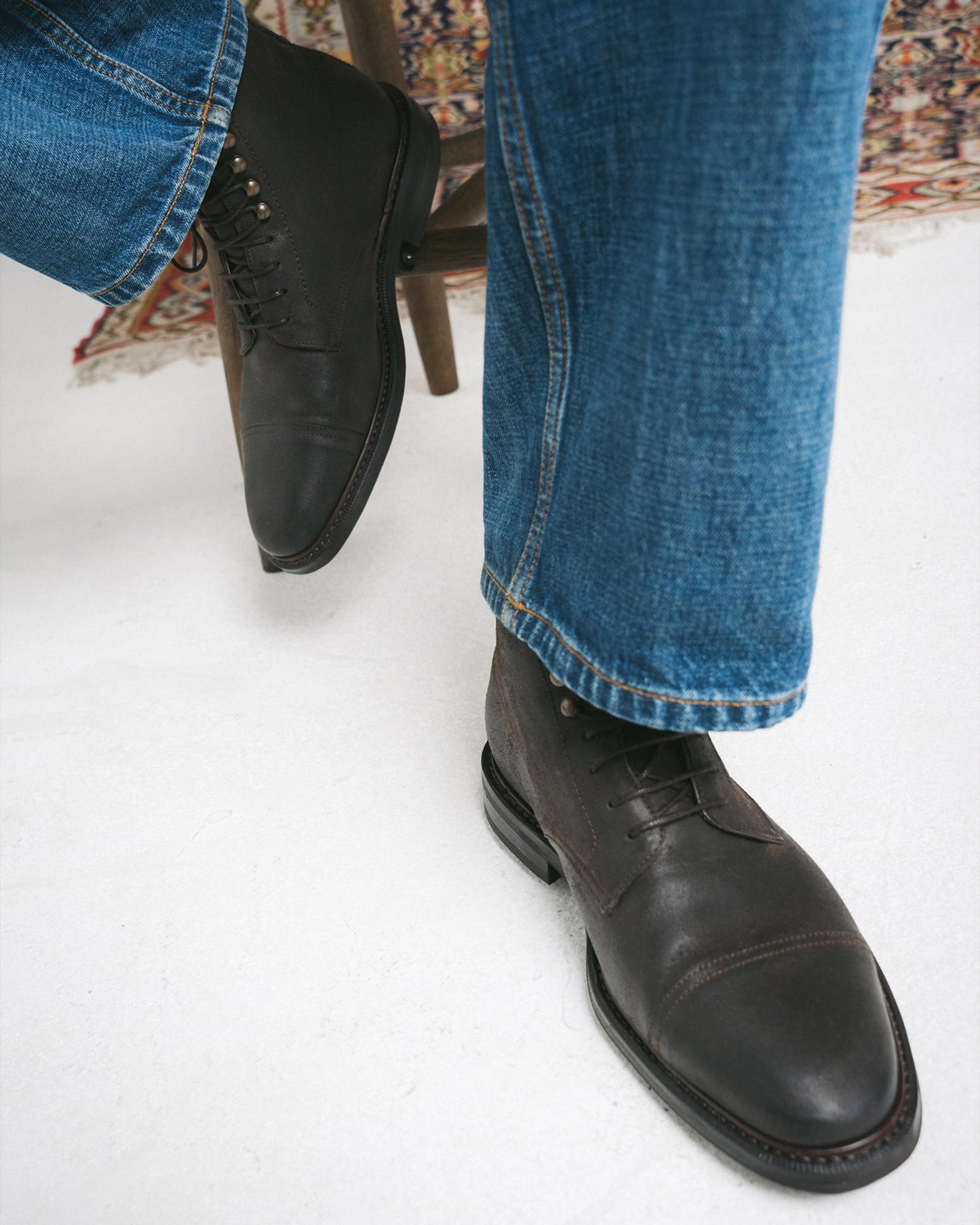 A person sitting on a chair wearing Abisko – Brown Waxed Suede boots with blue jeans.