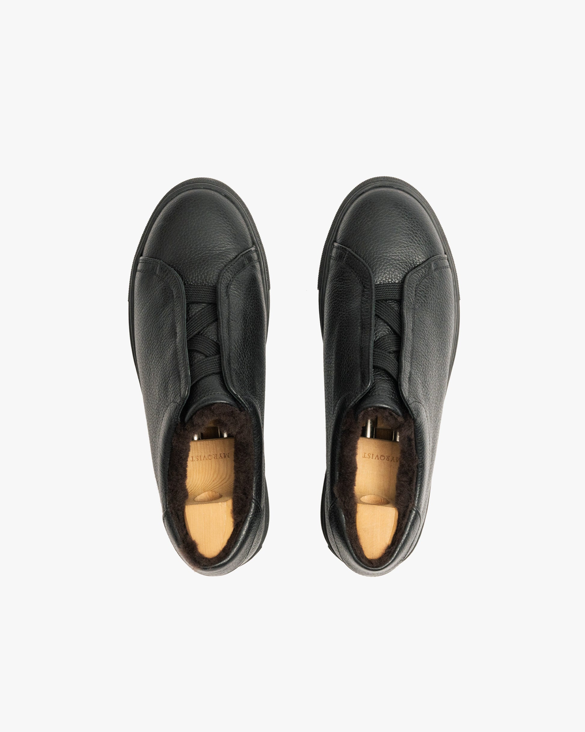A top-down shot of a pair of Alnö Shearling – Black Natural Grain sneakers fitted with wooden shoe trees.