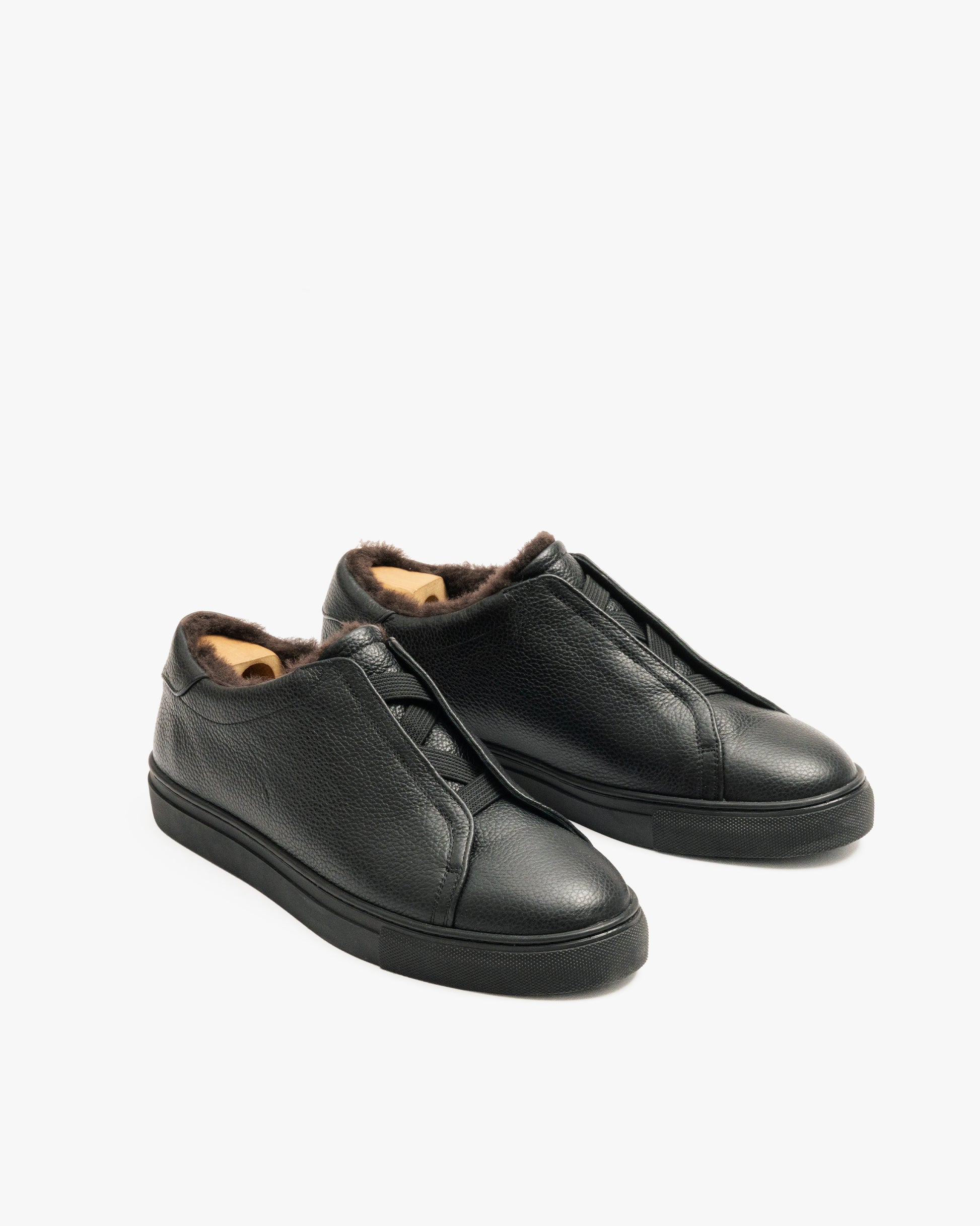 A pair of Alnö Shearling – Black Natural Grain sneakers fitted with wooden shoe trees, shot against a white background.