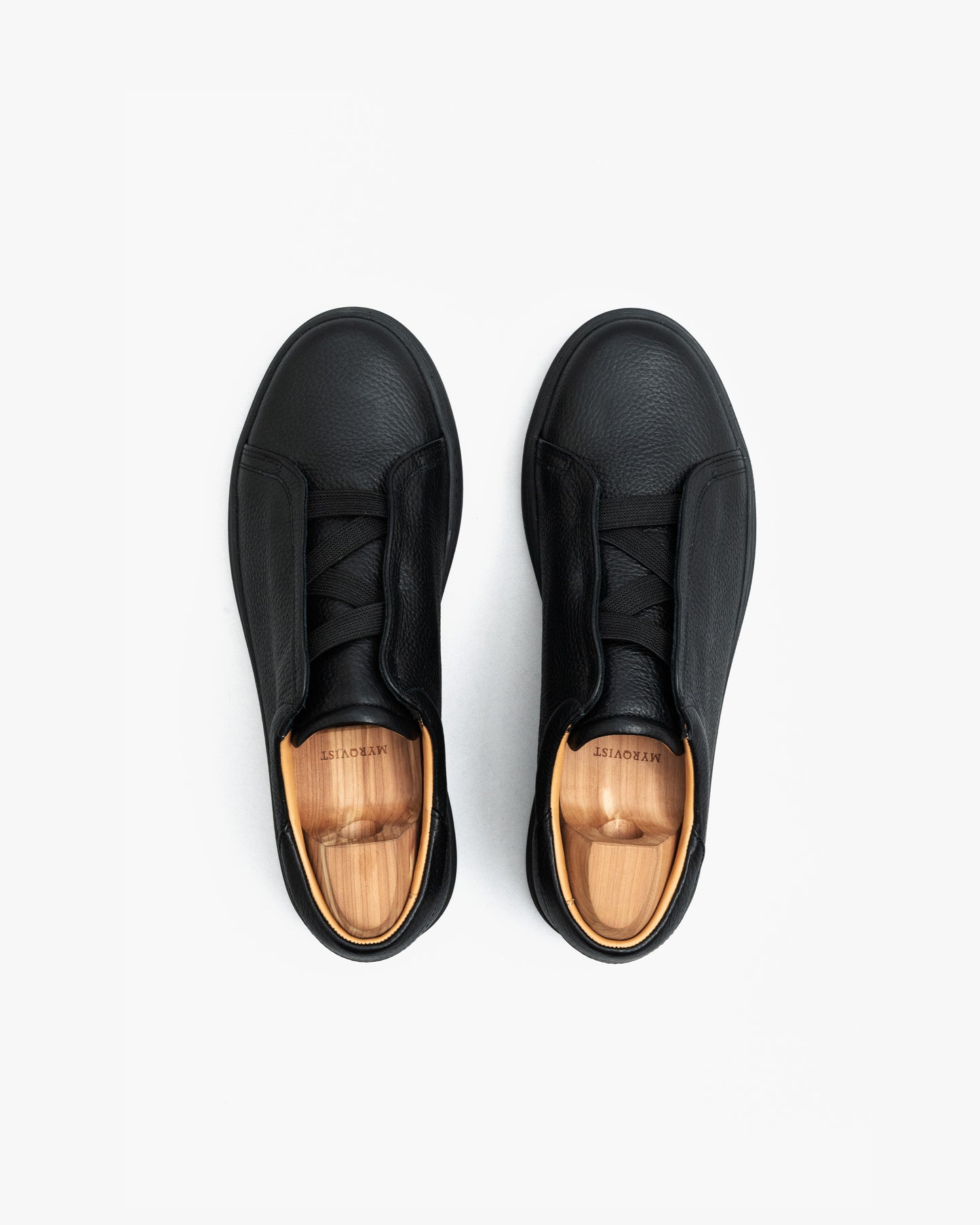 Pair of Alnö Monochrome II sneakers in black natural grain leather shown from above, highlighting the seamless monochrome design, textured finish, and wooden shoe trees inside each shoe.