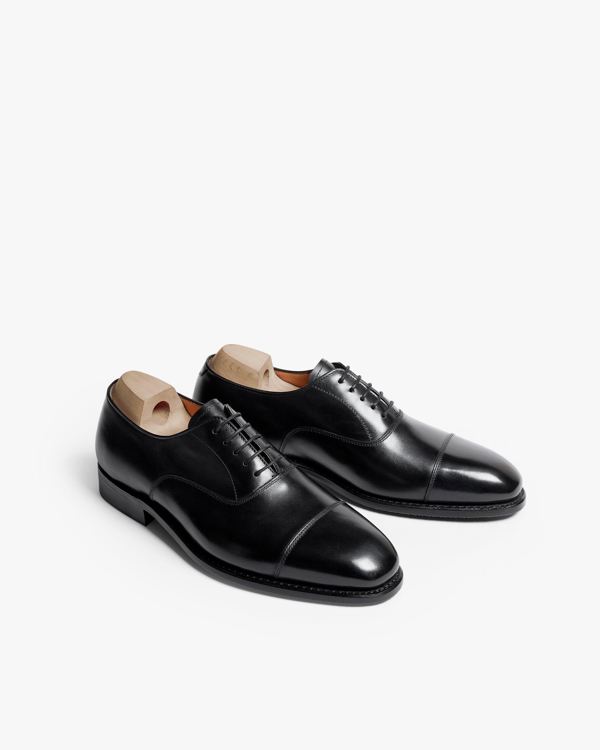 A pair of Äppelviken II – Black Calf cap toe oxfords with wooden shoe trees inside, shown at an angle on a white background.