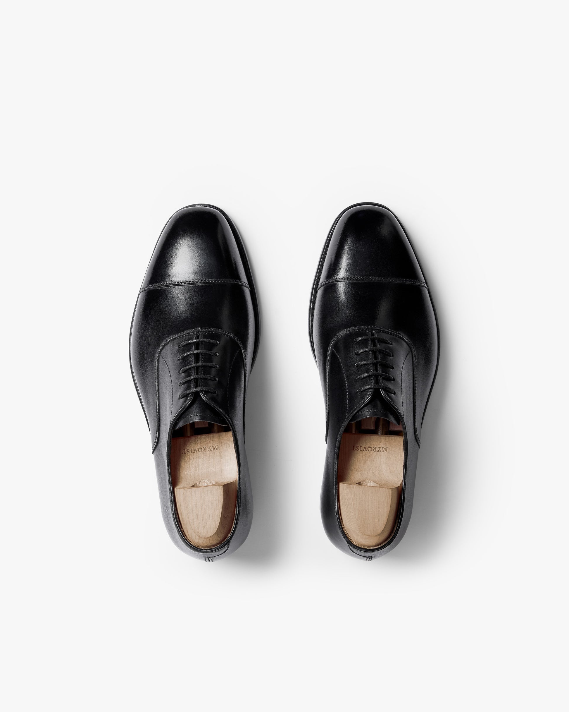 Top-down view of a pair of Äppelviken II – Black Calf oxford shoes with a cap toe and wooden shoe trees inside.