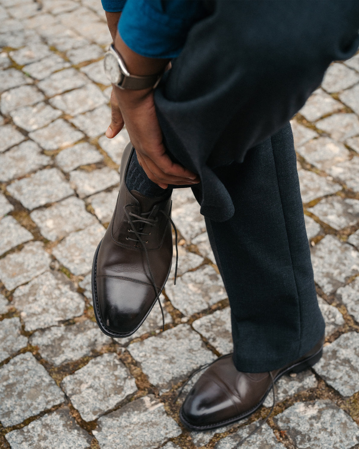 Äppelviken II – Dark Brown Calf cap-toe Oxford shoes worn with dark slacks on a cobblestone street.