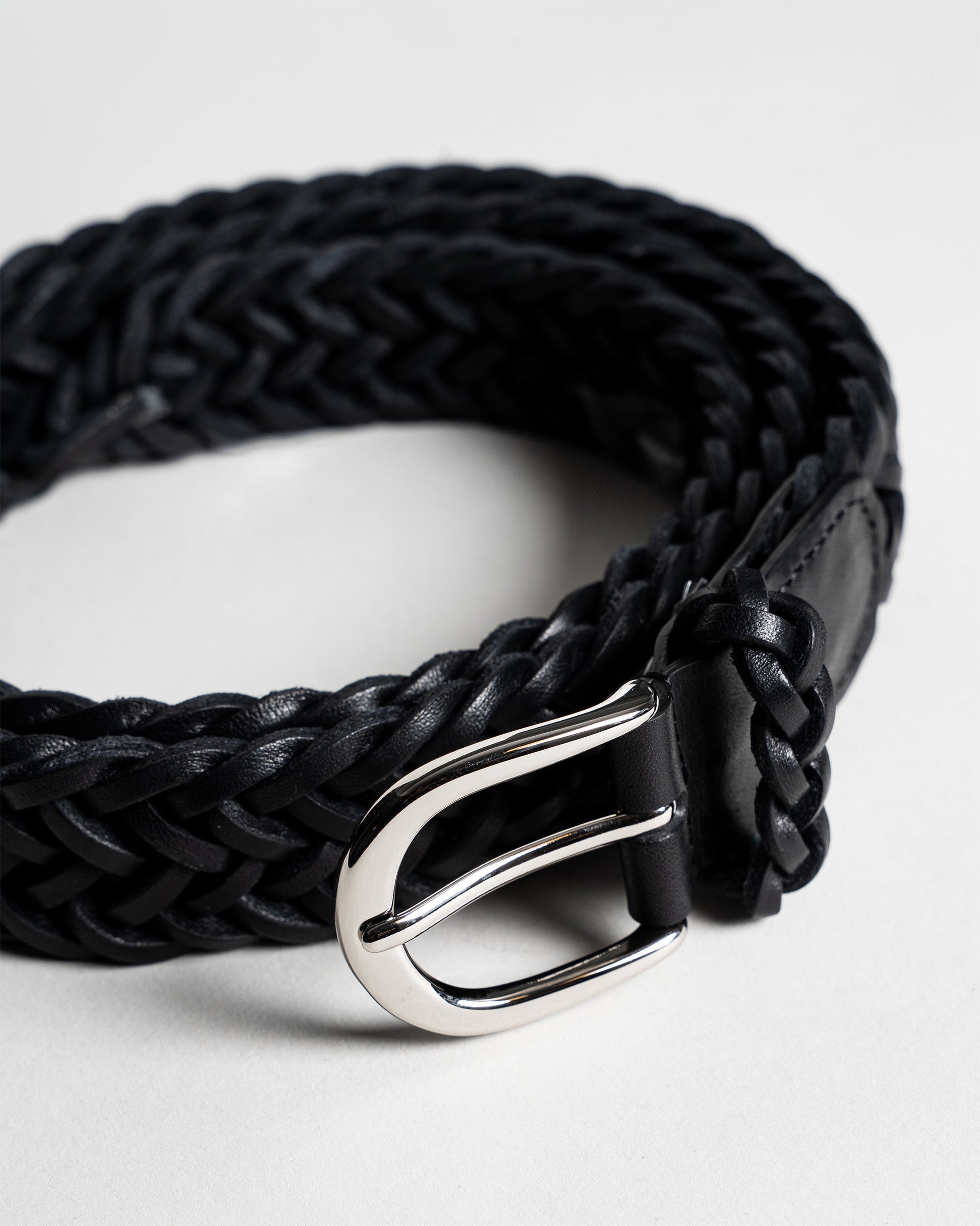 A close-up shot of Belt – Braided Black Leather, coiled to showcase the intricate weave and the polished silver buckle.
