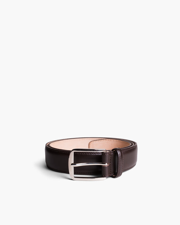 Men’s dark brown leather belt with a polished silver square buckle, featuring even stitching and softly contoured edges, styled in a coiled position against a white background.