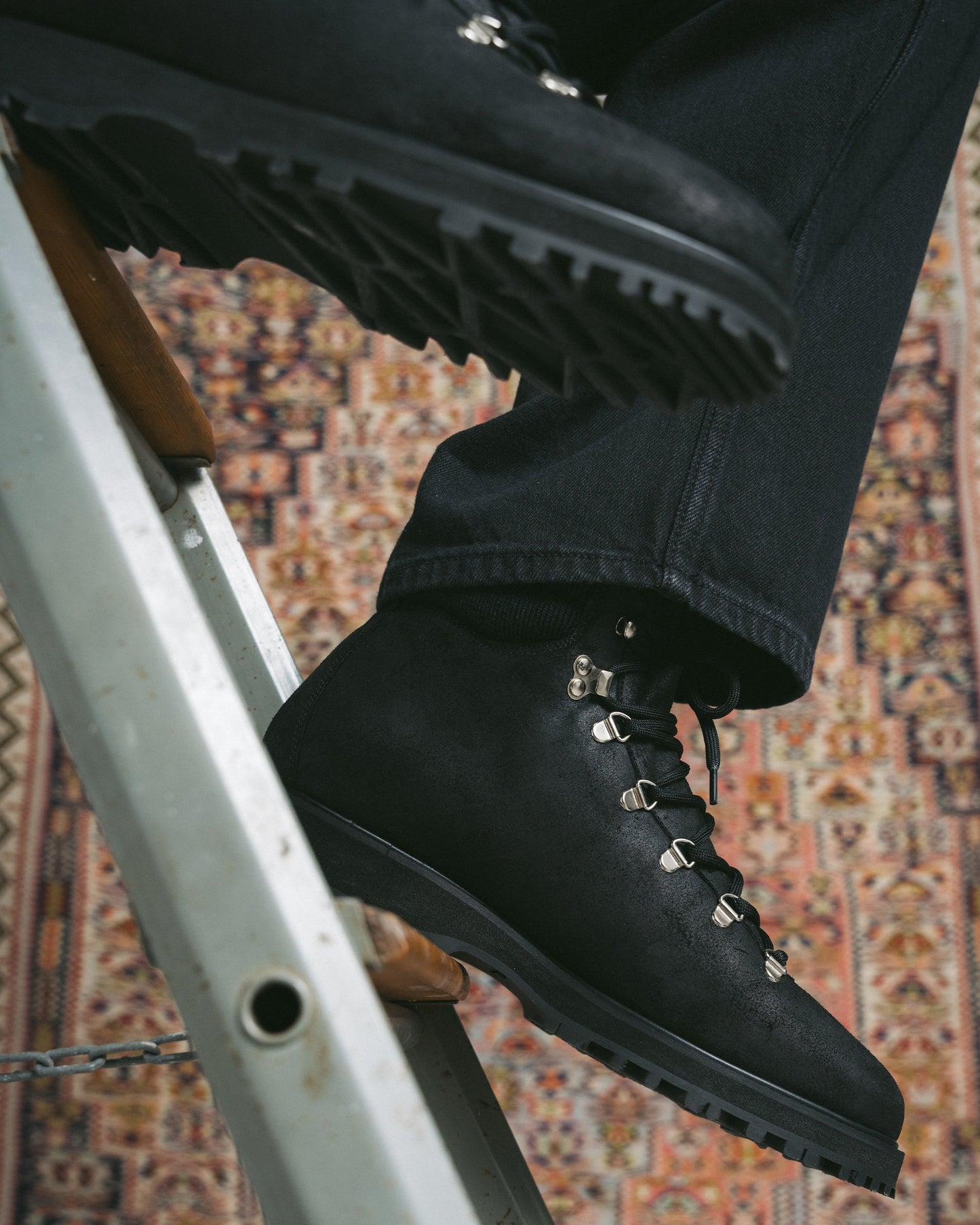 Close-up of a person wearing Duved II – Black Waxed Suede boots with black jeans while climbing a ladder.