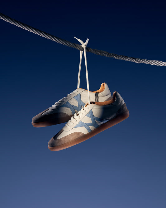 Högalid in white natural grain hanging by their laces from a metal cable against a deep blue sky backdrop.