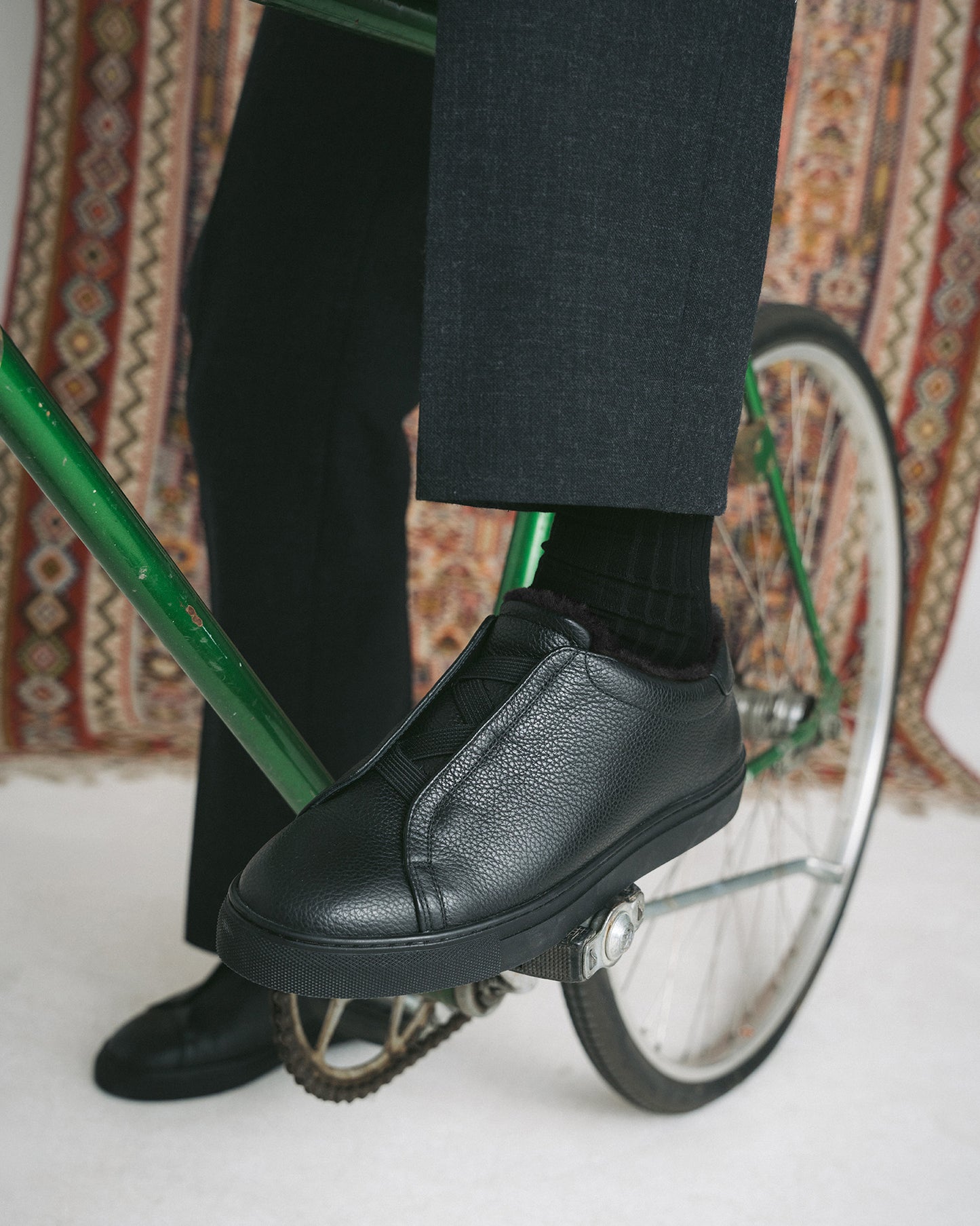 Close-up of Alnö Shearling – Black Natural Grain sneakers on the pedal of a green bicycle.