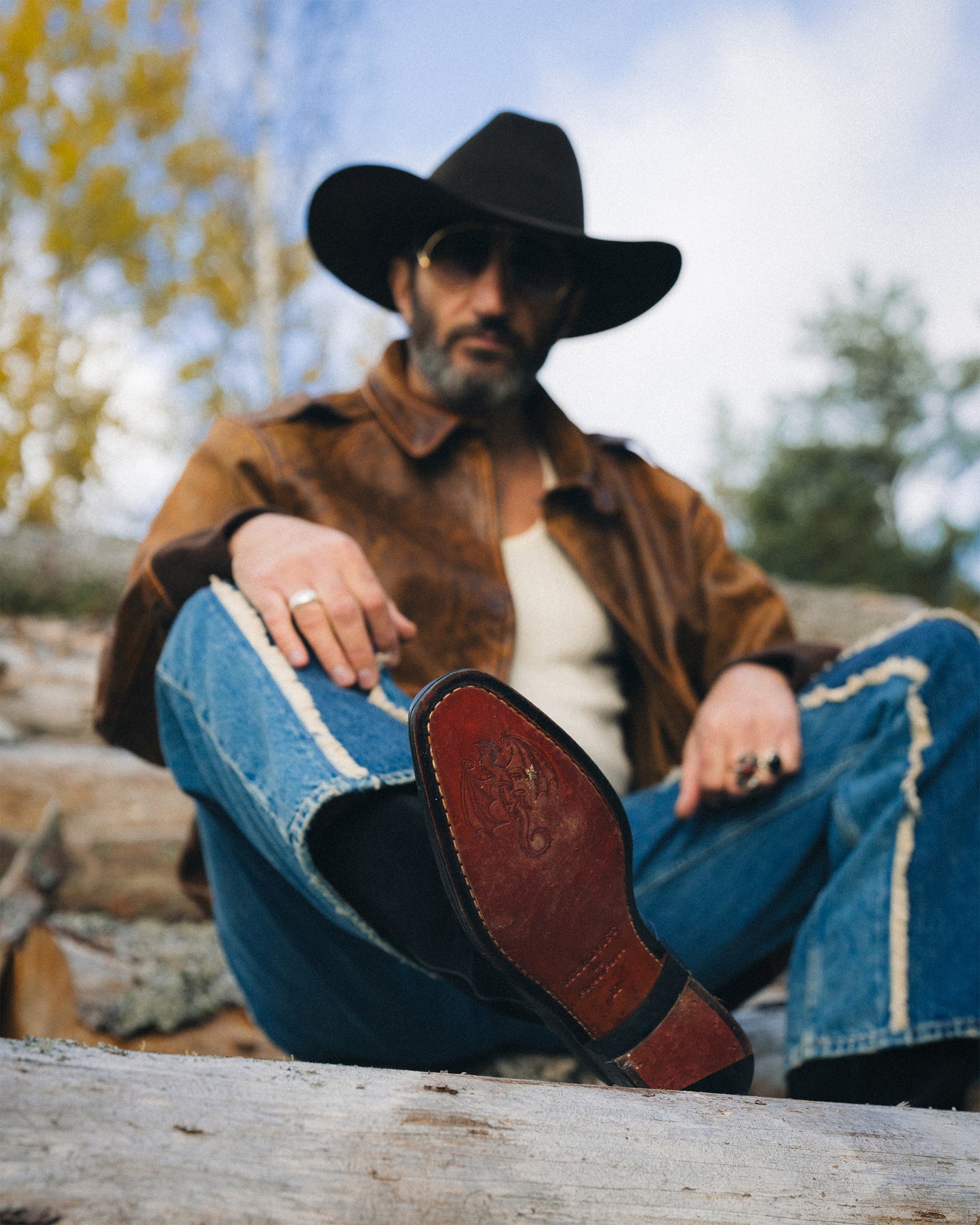 Fares Fares relaxes on a log, showing the intricate dragon crest on the leather sole of Karlslund – Fares Edition boots.