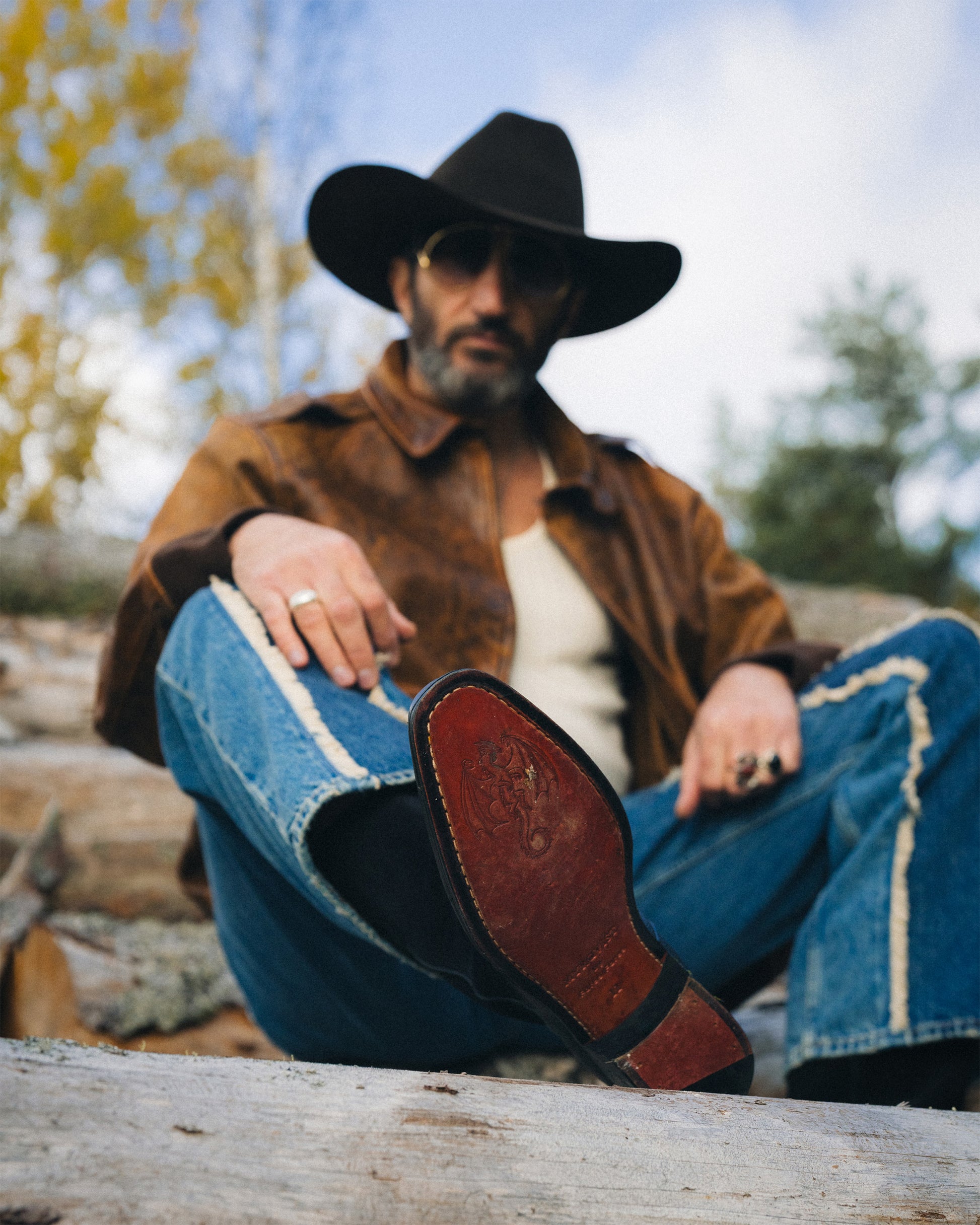 Fares Fares relaxes on a log, showing the intricate dragon crest on the leather sole of Karlslund – Fares Edition boots.